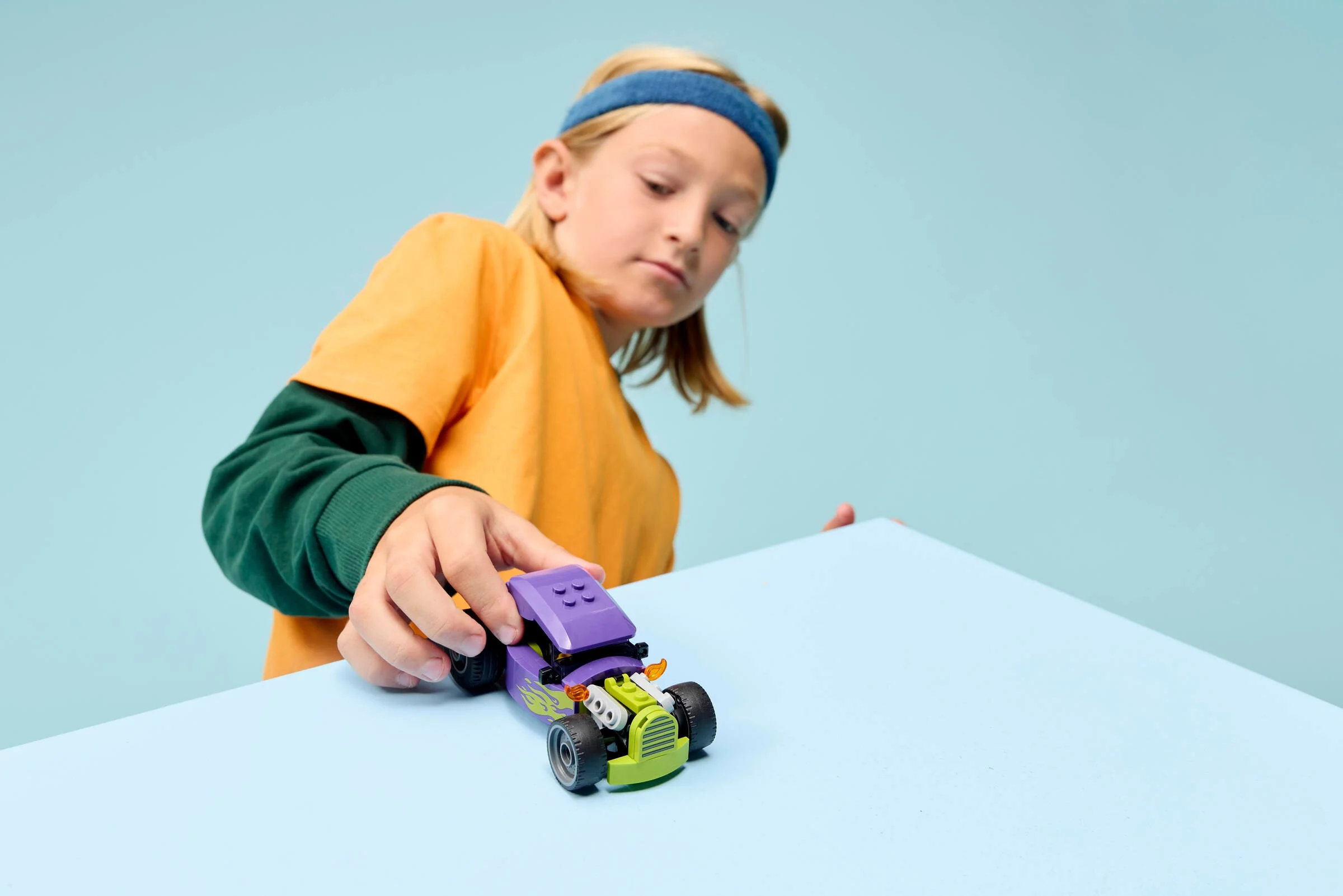 Un copil se joacă cu un hot rod LEGO, accent pe modelul construit.