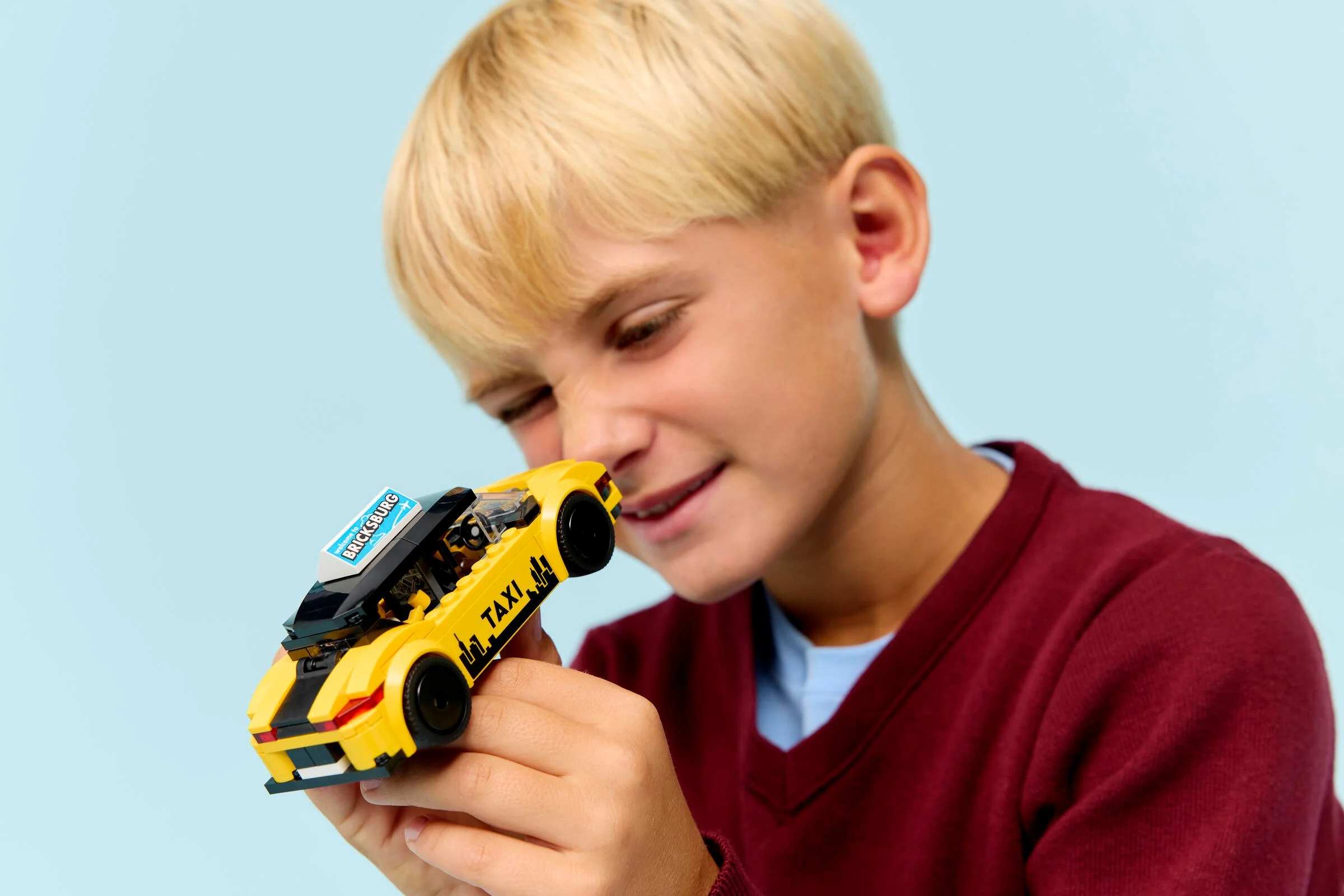Băiat admirând taxiul galben LEGO, cu atenție la detalii. Modelul este centrul atenției.