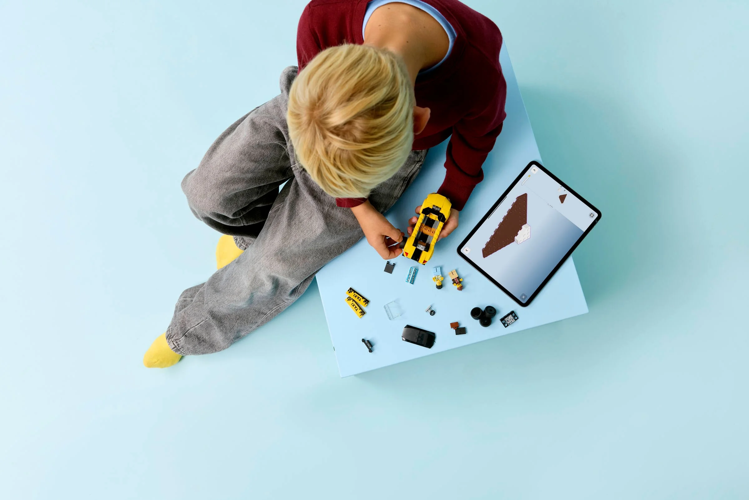 Băiat construind un taxi LEGO galben cu instrucțiuni pe tabletă. Joacă creativă cu jucării.