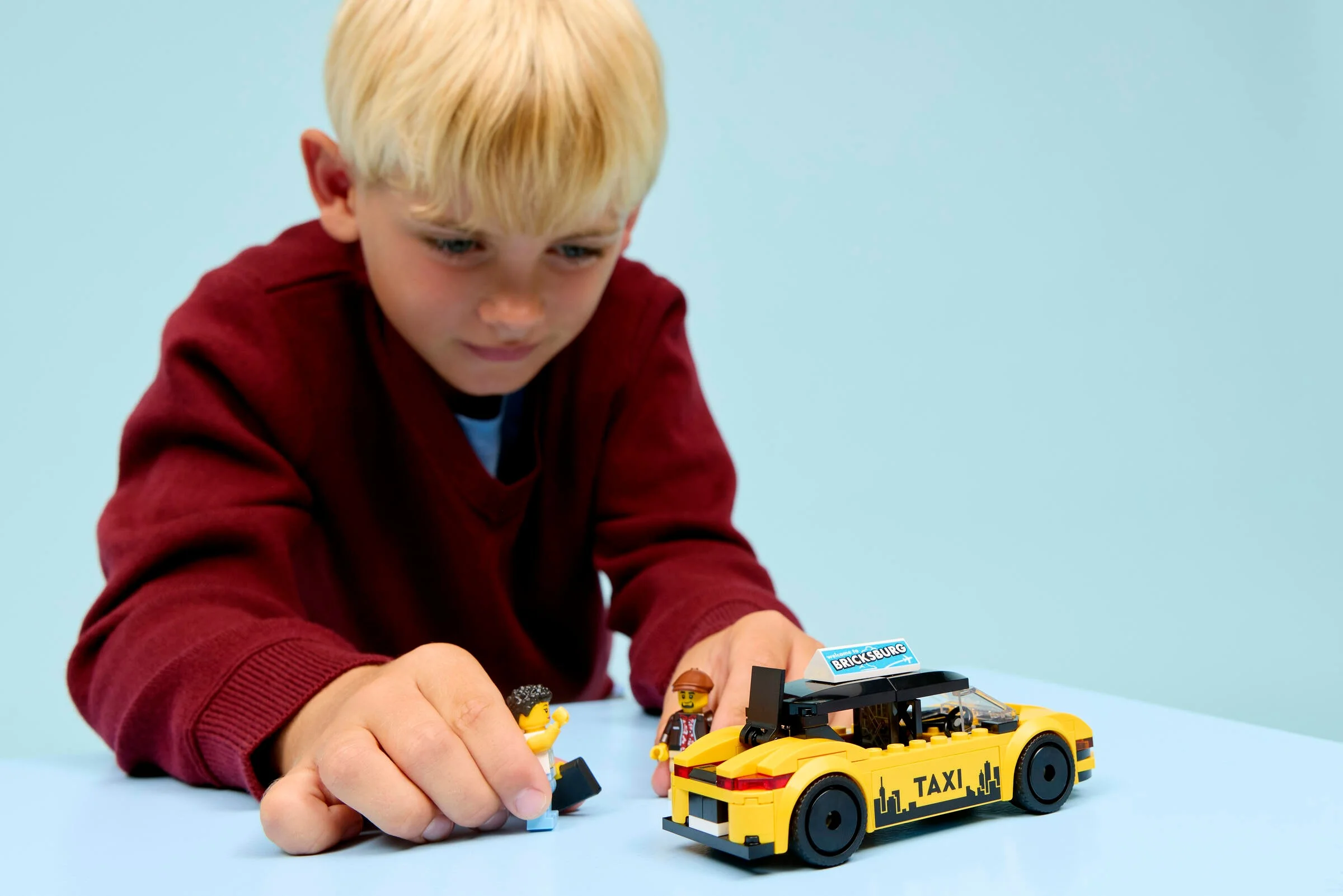 Copil se joacă cu taxiul galben LEGO City 60487 și minifigurinele incluse.