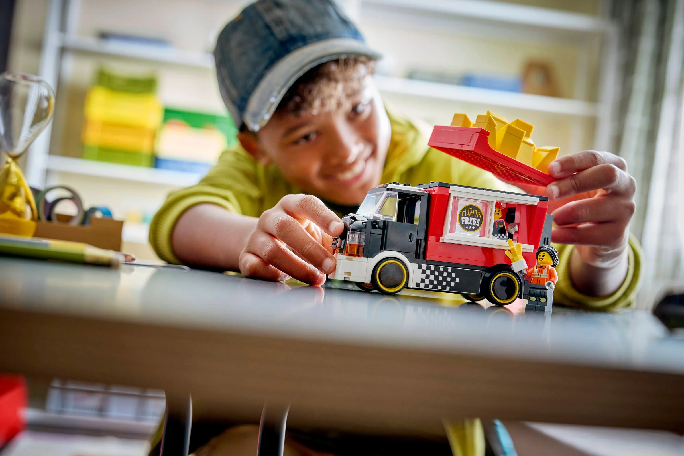 Un copil zâmbește în timp ce se joacă cu camionul de cartofi prăjiți LEGO City 60488.