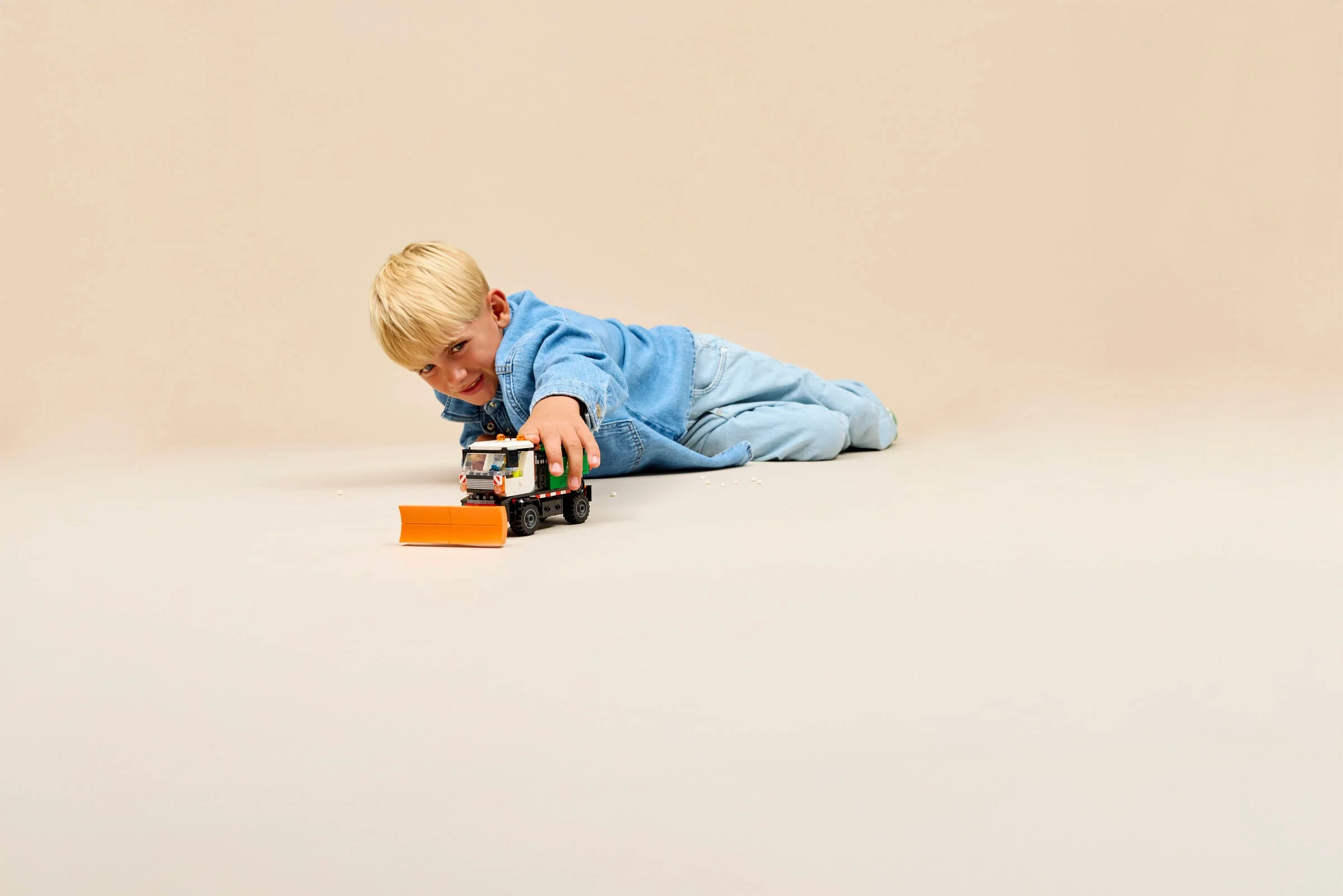 Copil se joacă cu plugul de zăpadă LEGO, întins pe podea. Joacă creativă și distractivă.