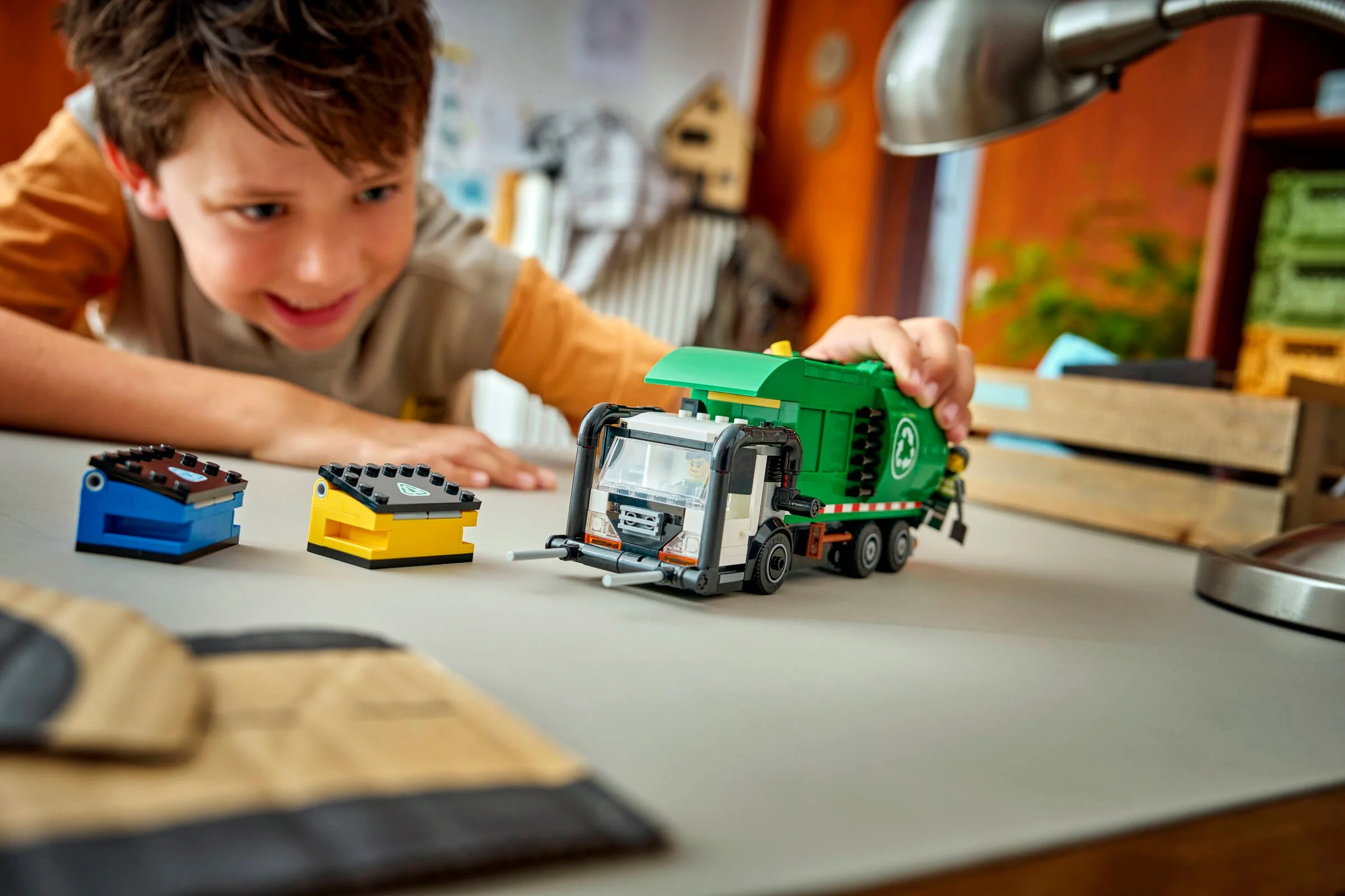 Un băiat se joacă cu camionul de reciclare LEGO City, aruncând containerele în el.