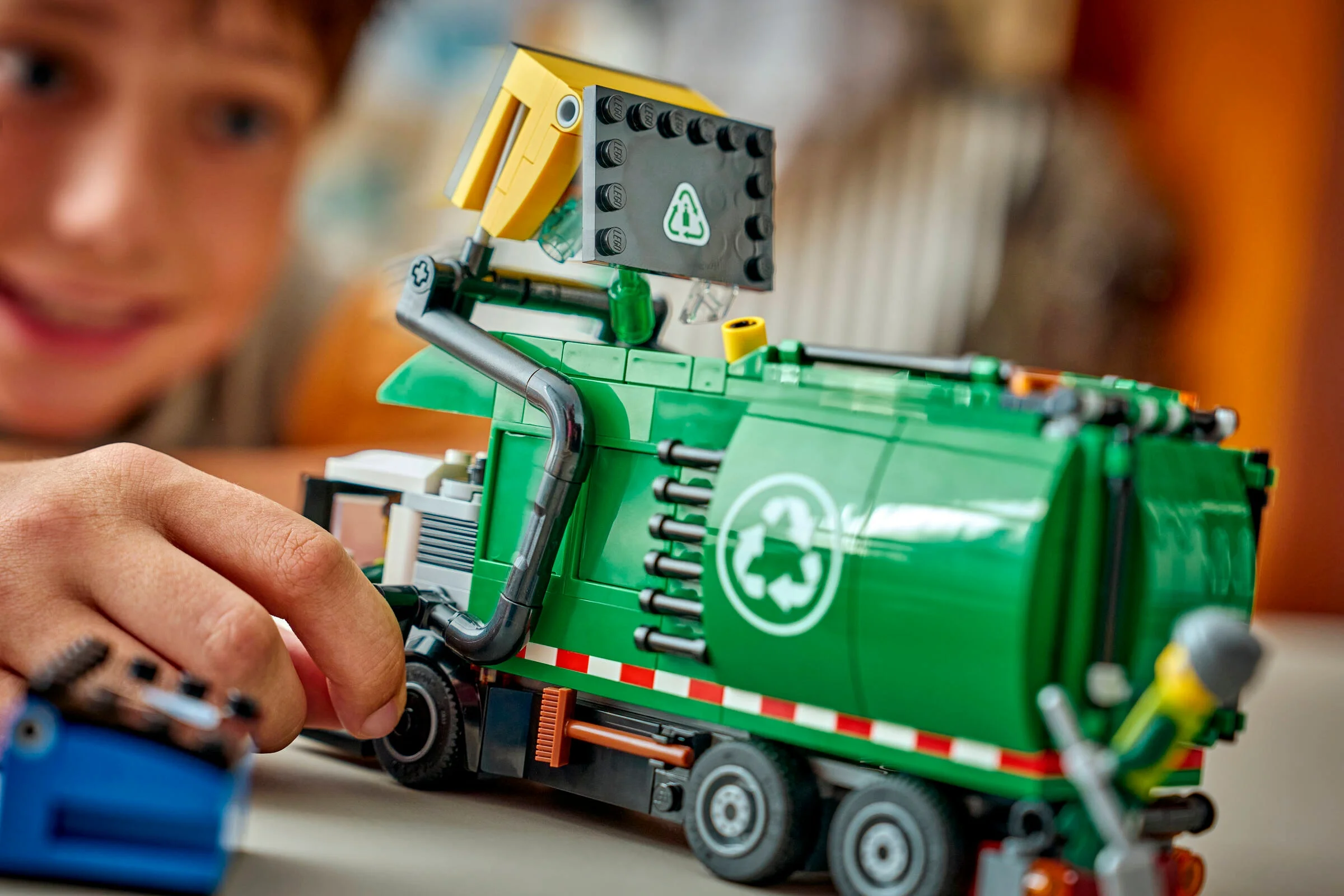 Camionul de reciclare LEGO City 60495 în acțiune, cu un copil bucuros în fundal.
