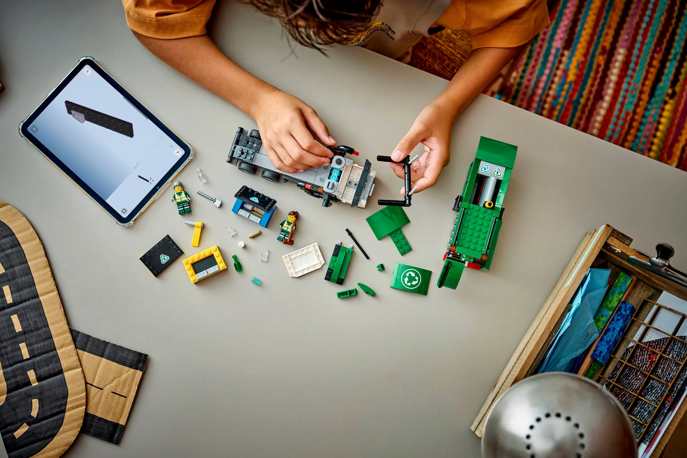 Un copil construiește camionul de reciclare LEGO 60495, folosind instrucțiuni digitale pe o tabletă.
