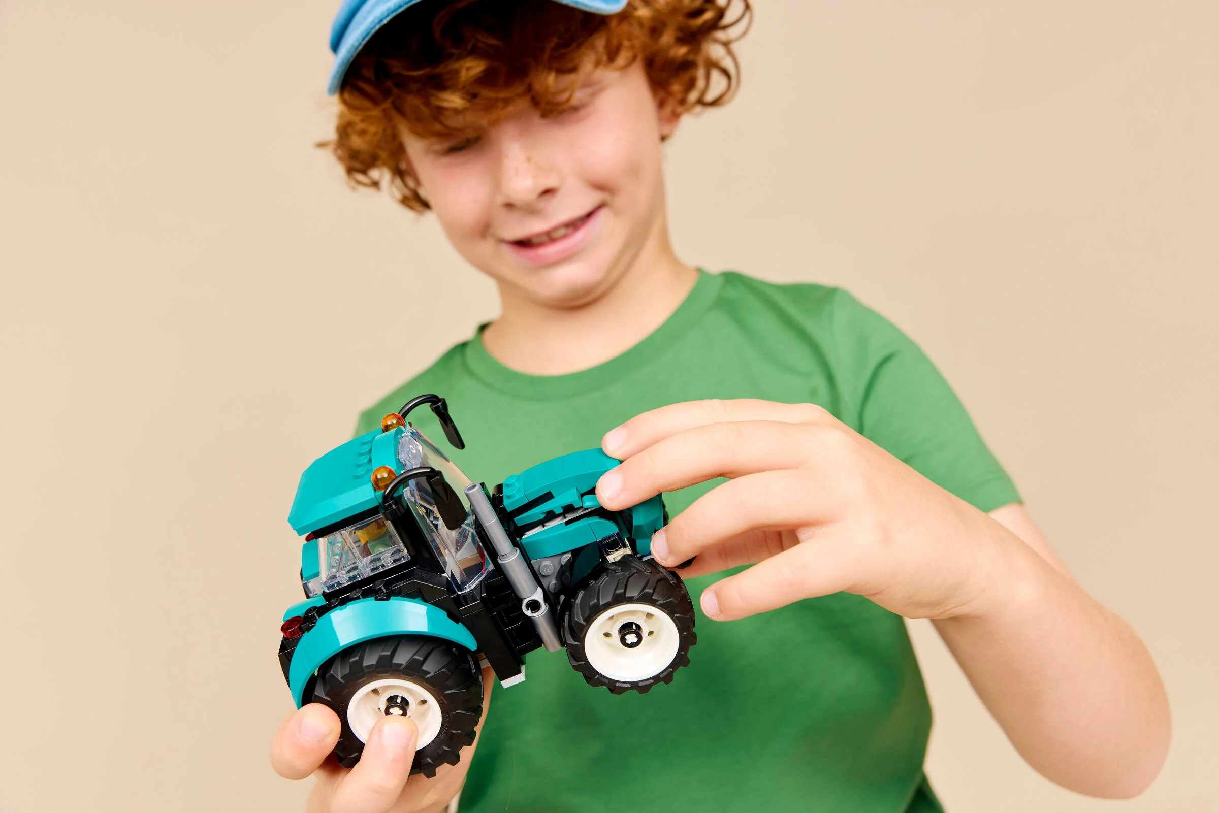 Băiat zâmbitor ține în mâini tractorul LEGO, arătând modelul construit.