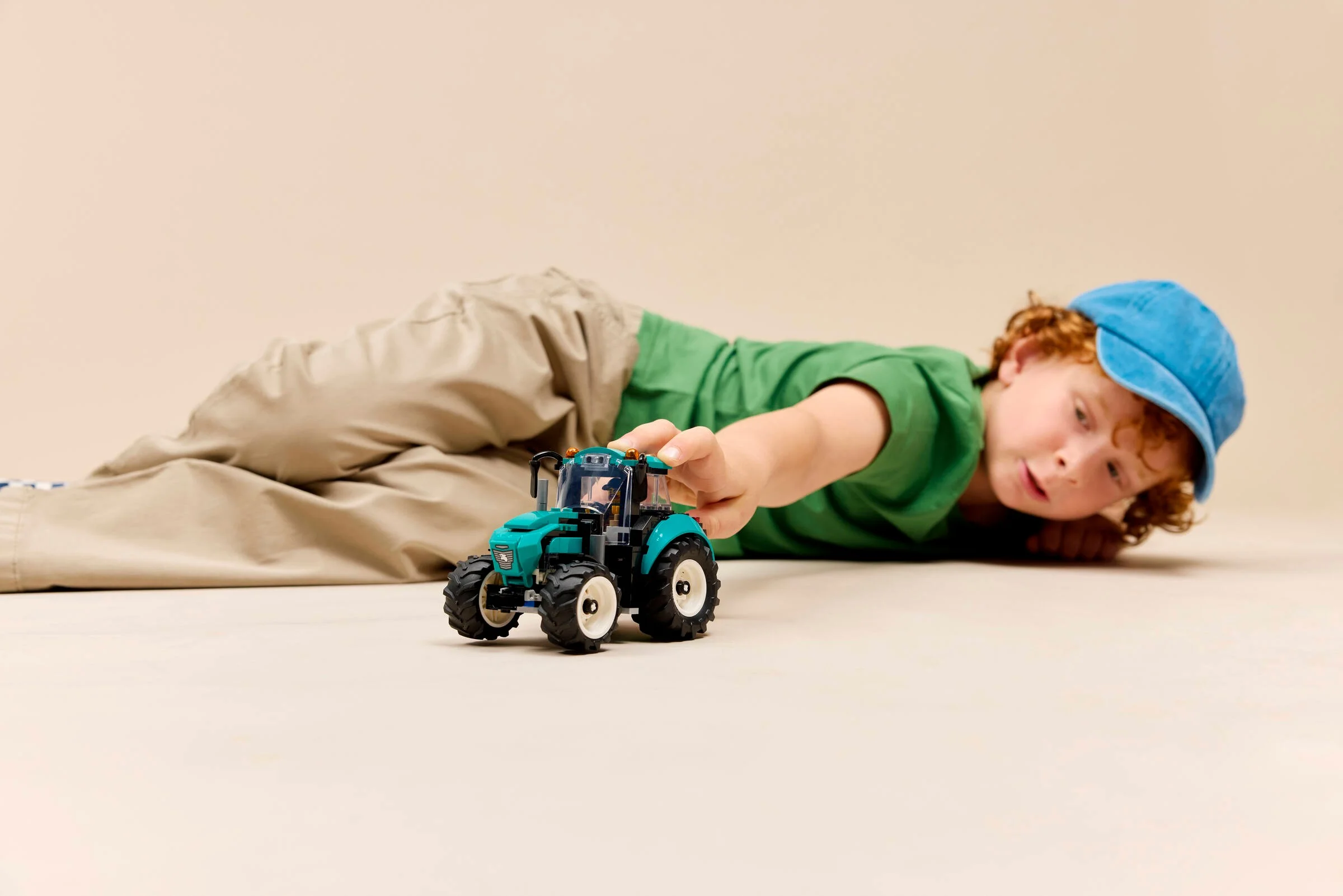 Copil se joacă cu tractorul LEGO City 60498 pe podea, ilustrând creativitatea.