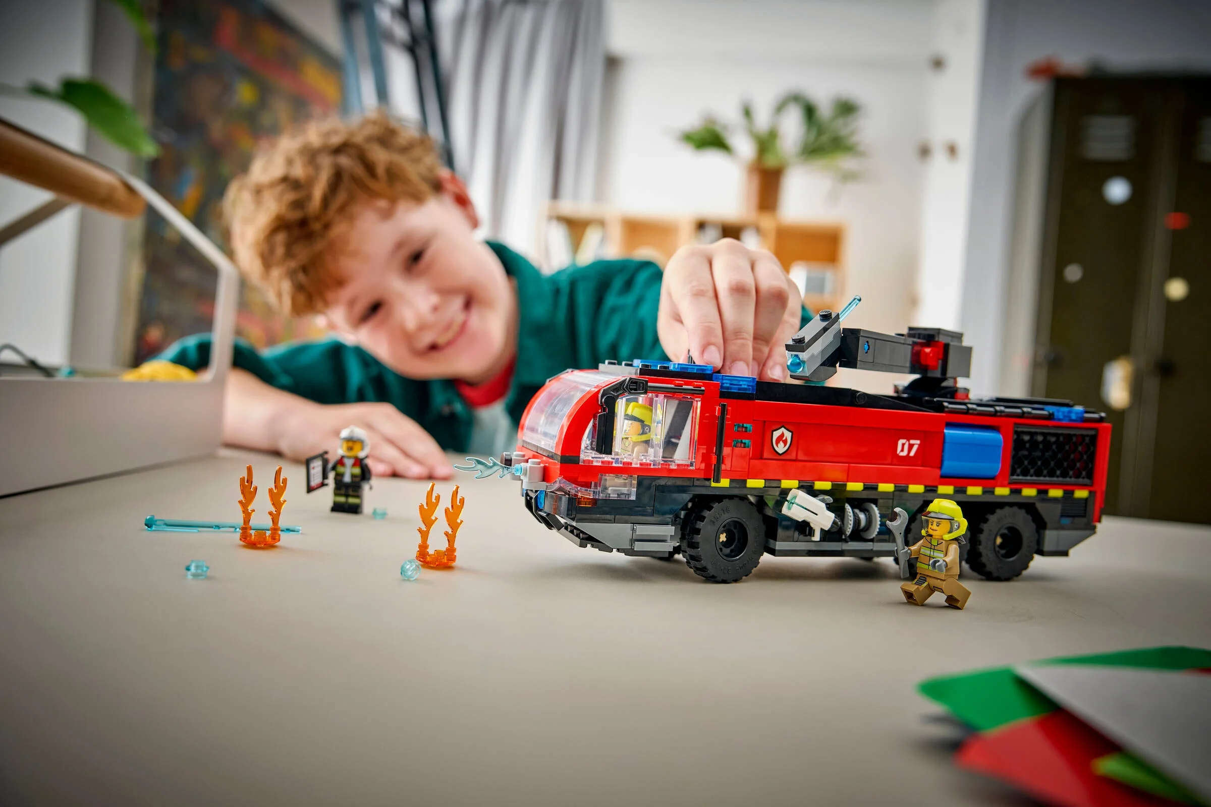 Băiat zâmbitor se joacă cu camionul de pompieri LEGO. Distracție garantată! 