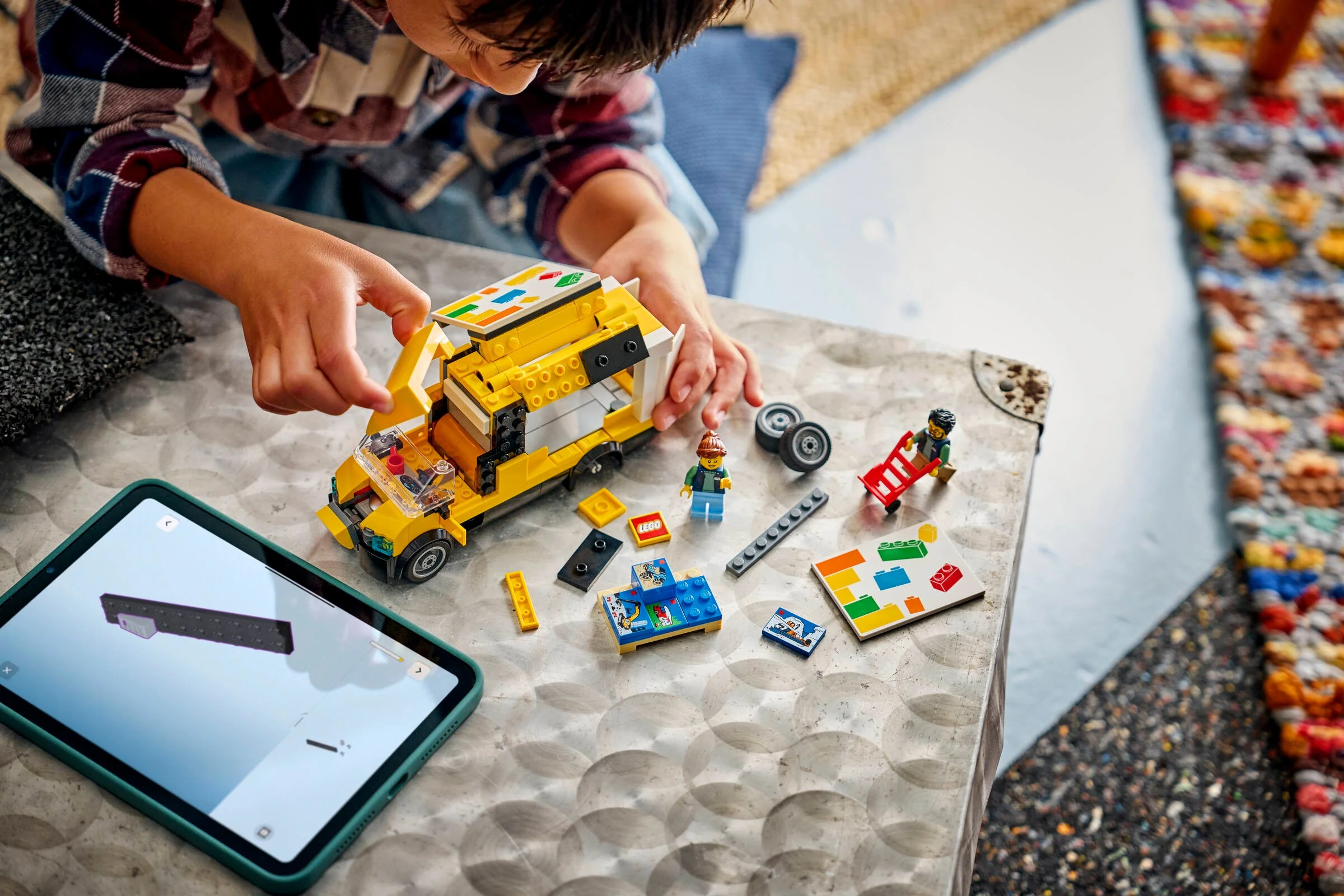 Copil construind furgoneta LEGO galbenă, urmând instrucțiunile de pe tabletă. Setul include minifigurine.