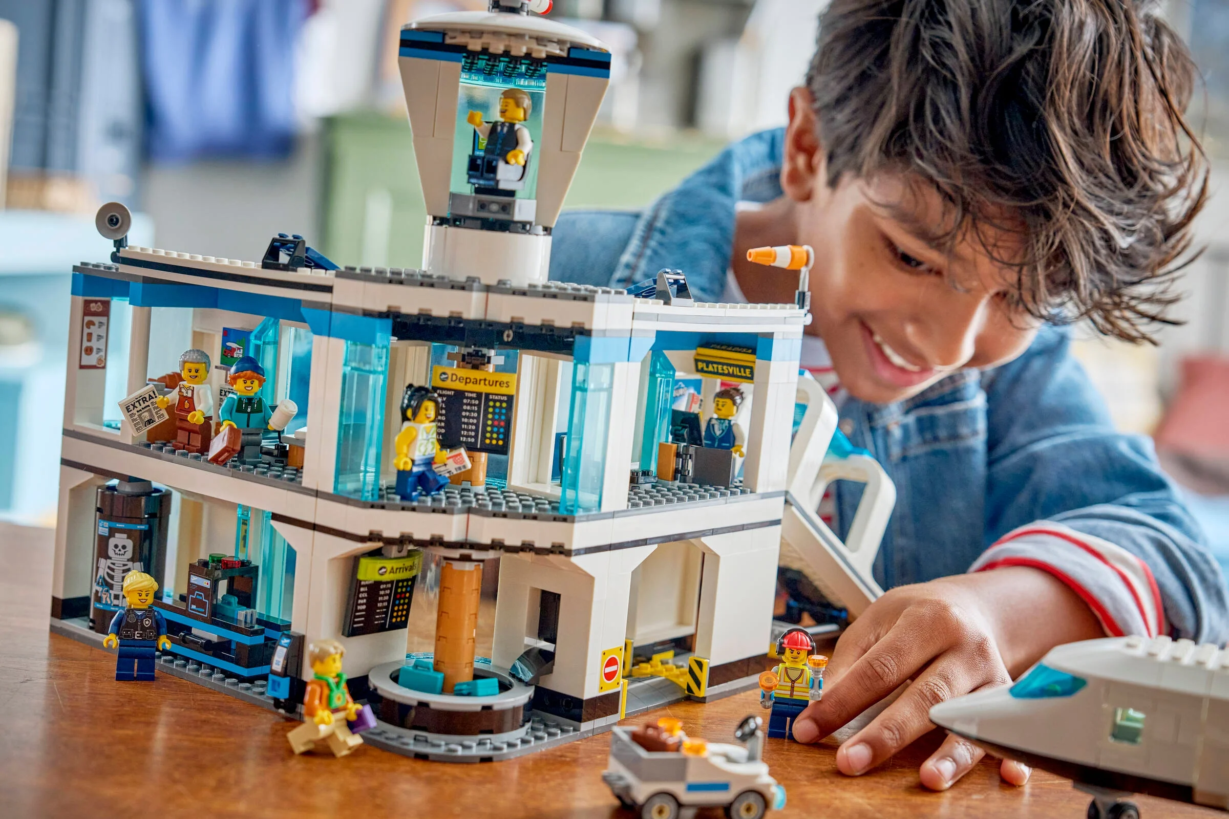 Băiat zâmbitor se joacă cu aeroportul LEGO City, explorând fiecare detaliu al setului.