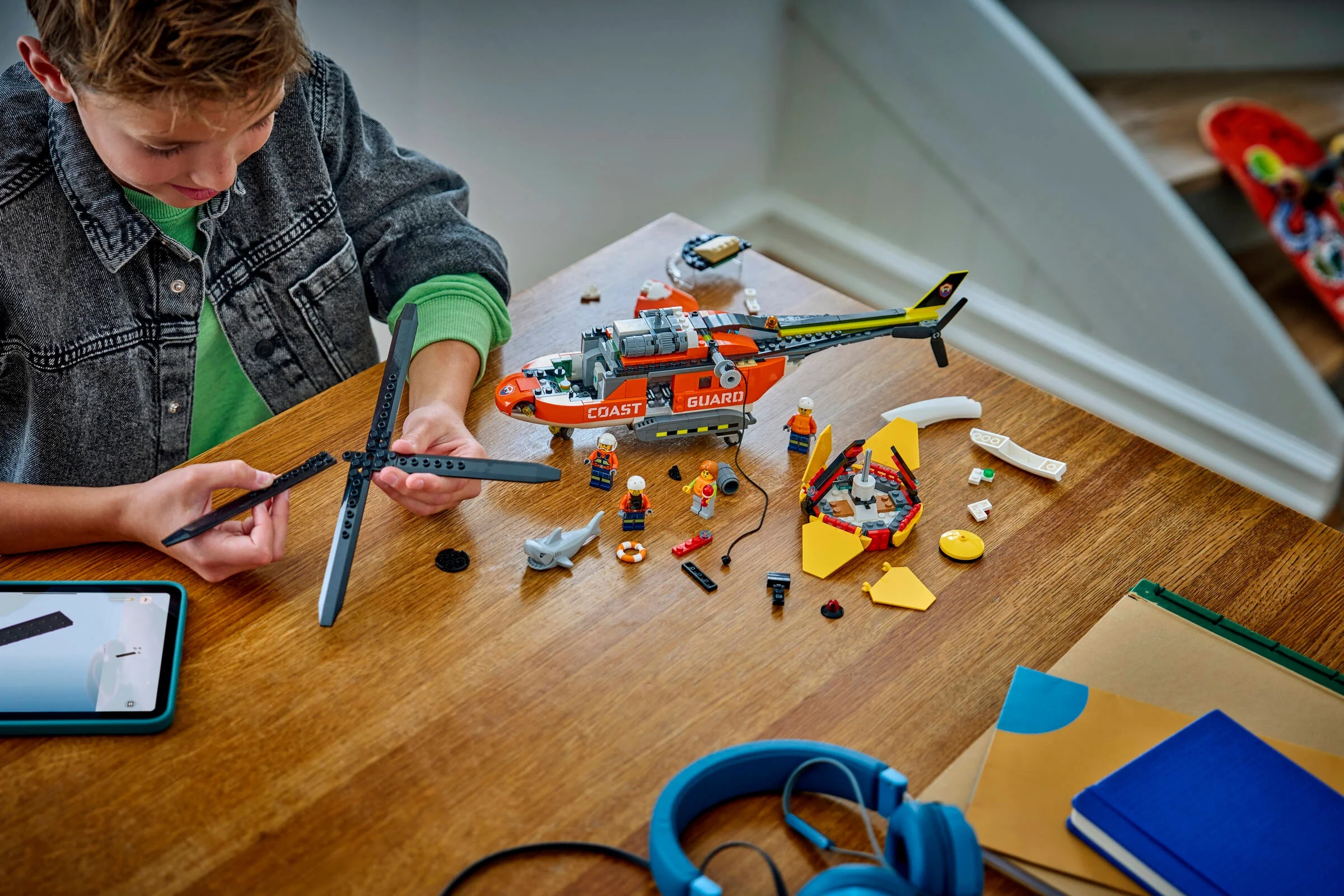 Băiat construind elicopterul LEGO de salvare pe masă. Piesele sunt aranjate ordonat. 