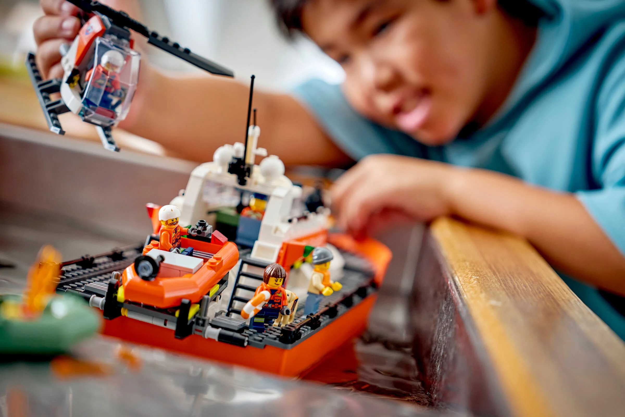 Copil se joacă cu barca de salvare și elicopterul LEGO Coast Guard.