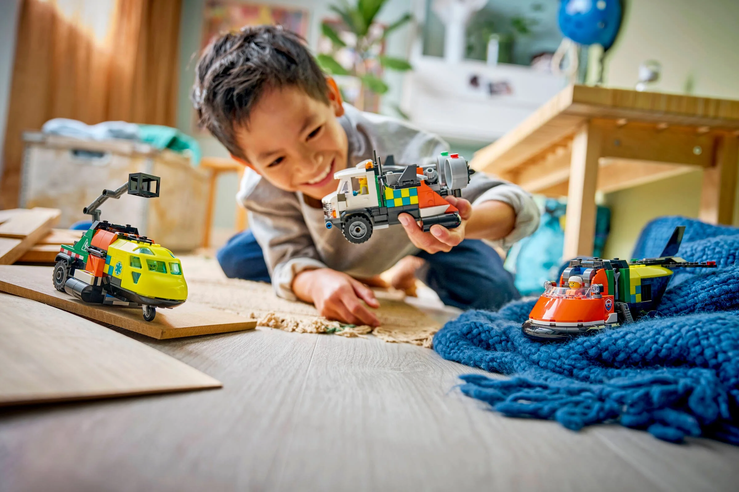 Copil zâmbitor se joacă cu camionul, hovercraftul și avionul LEGO City 60505.