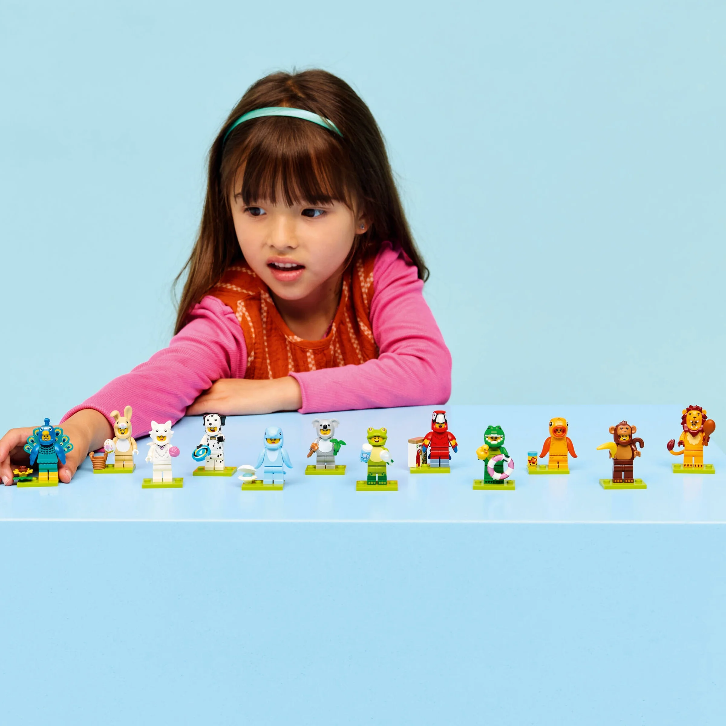 O fetiță se joacă cu minifigurinele costumate din seria LEGO 71051, pe un fundal albastru.