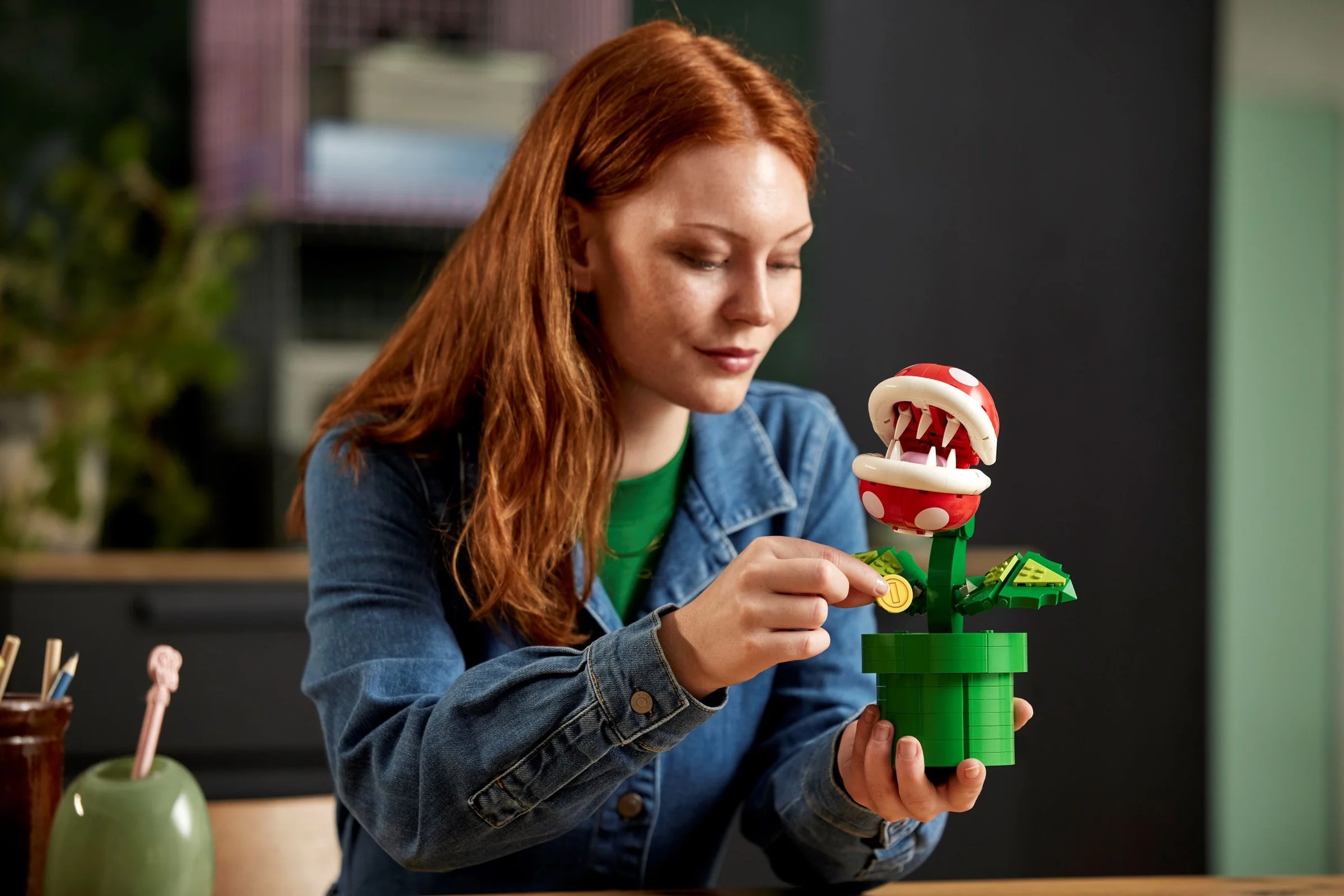O femeie interacționează cu planta Piranha LEGO, introducând o monedă în gură.