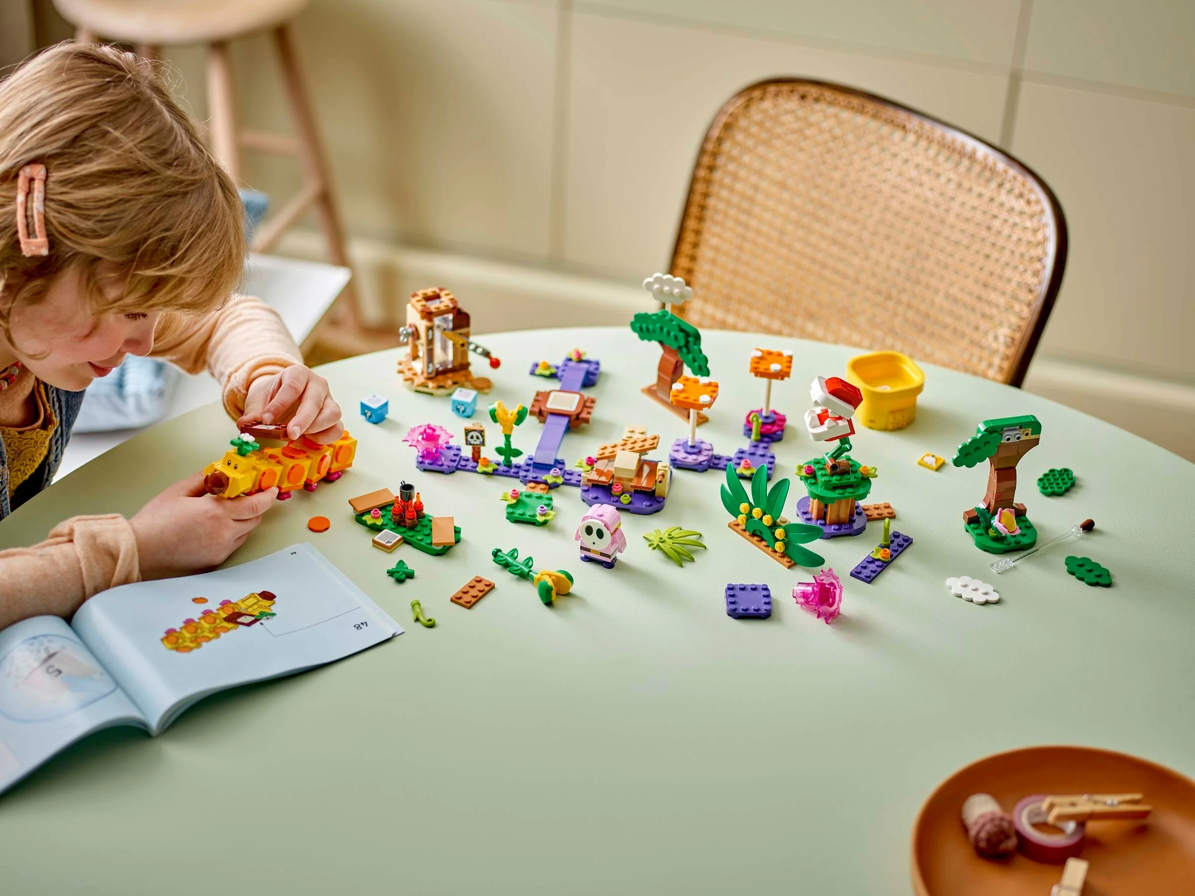 Imagine cu o fetiță construind setul LEGO Super Mario, Jungle Maker Set (71434), pe o masă verde.