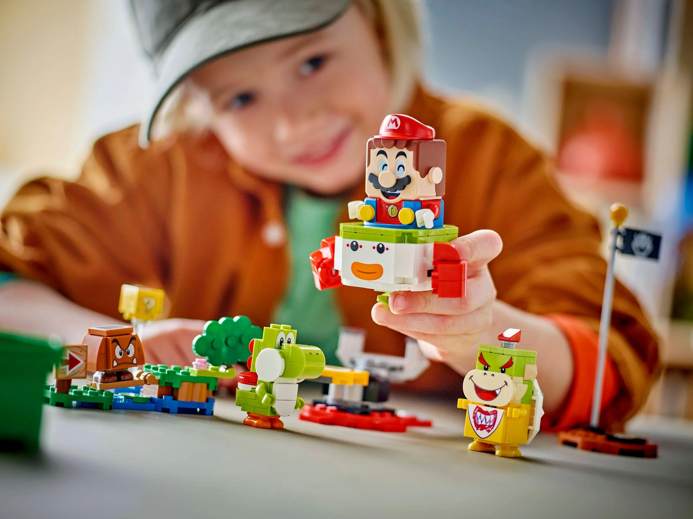Copil se joacă cu setul LEGO Mario. Personaje construite: Mario, Bowser Jr., Goomba, Yoshi.