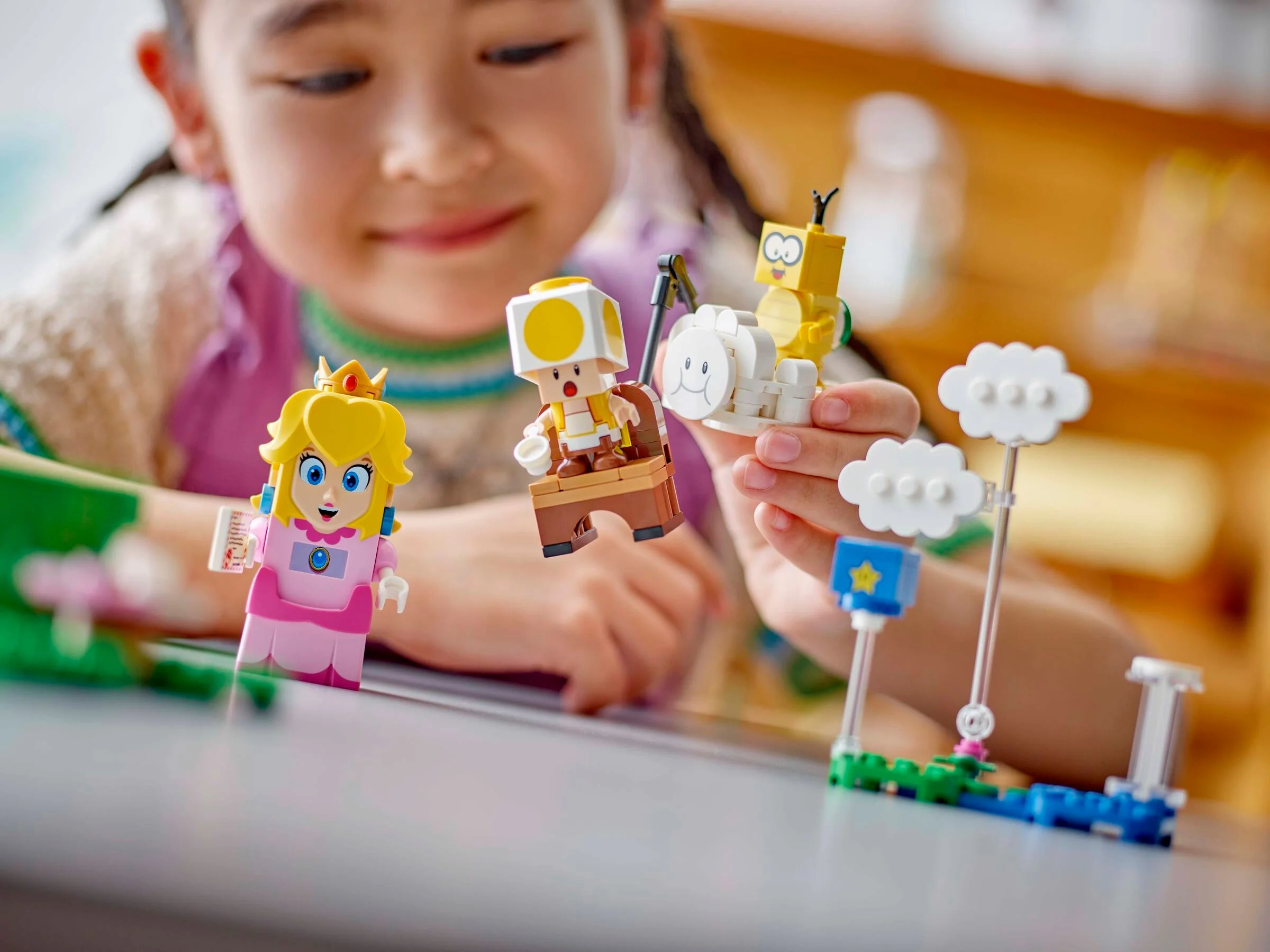 Fetiță interacționând cu figurinele LEGO Peach, Toad și Nabbit. Aventuri cu Super Mario.