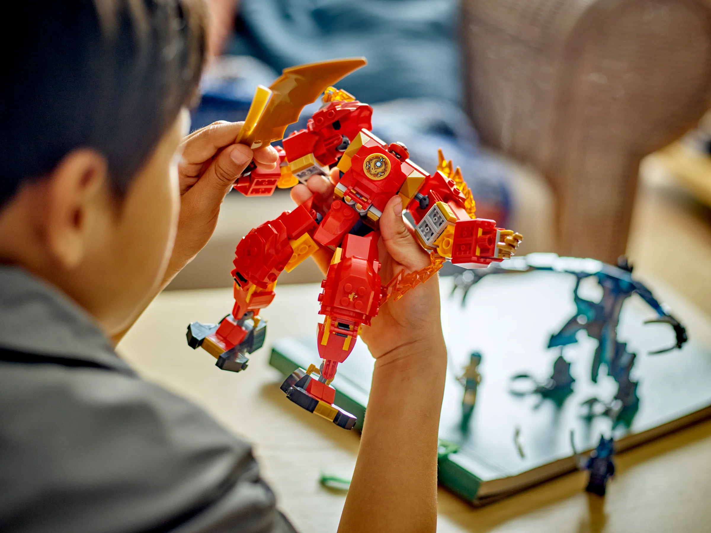 Băiat ținând în mână robotul de foc al lui Kai, un model LEGO Ninjago roșu și auriu.