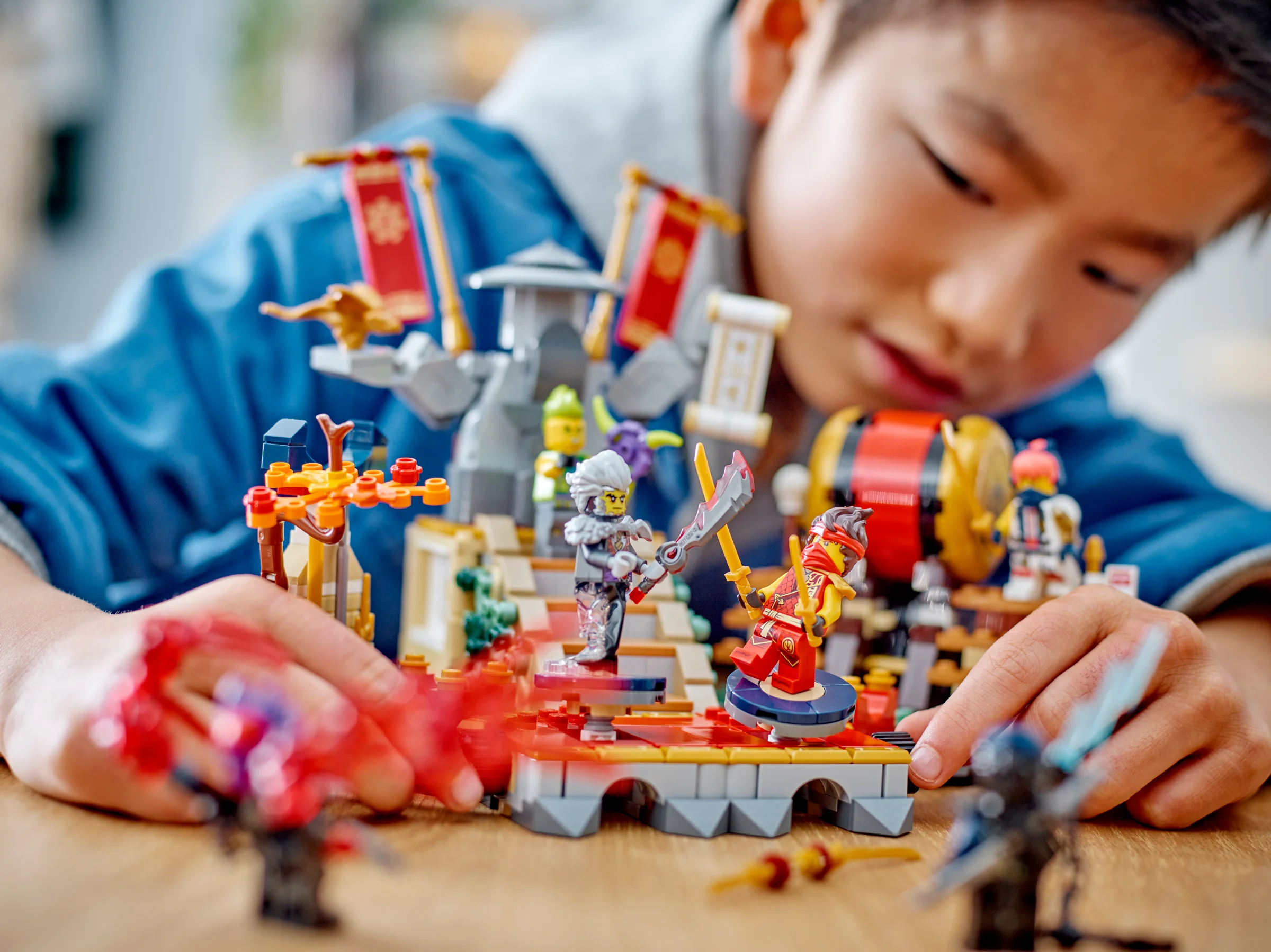 Băiat se joacă cu arena LEGO Ninjago, figurinele fiind în prim-plan.