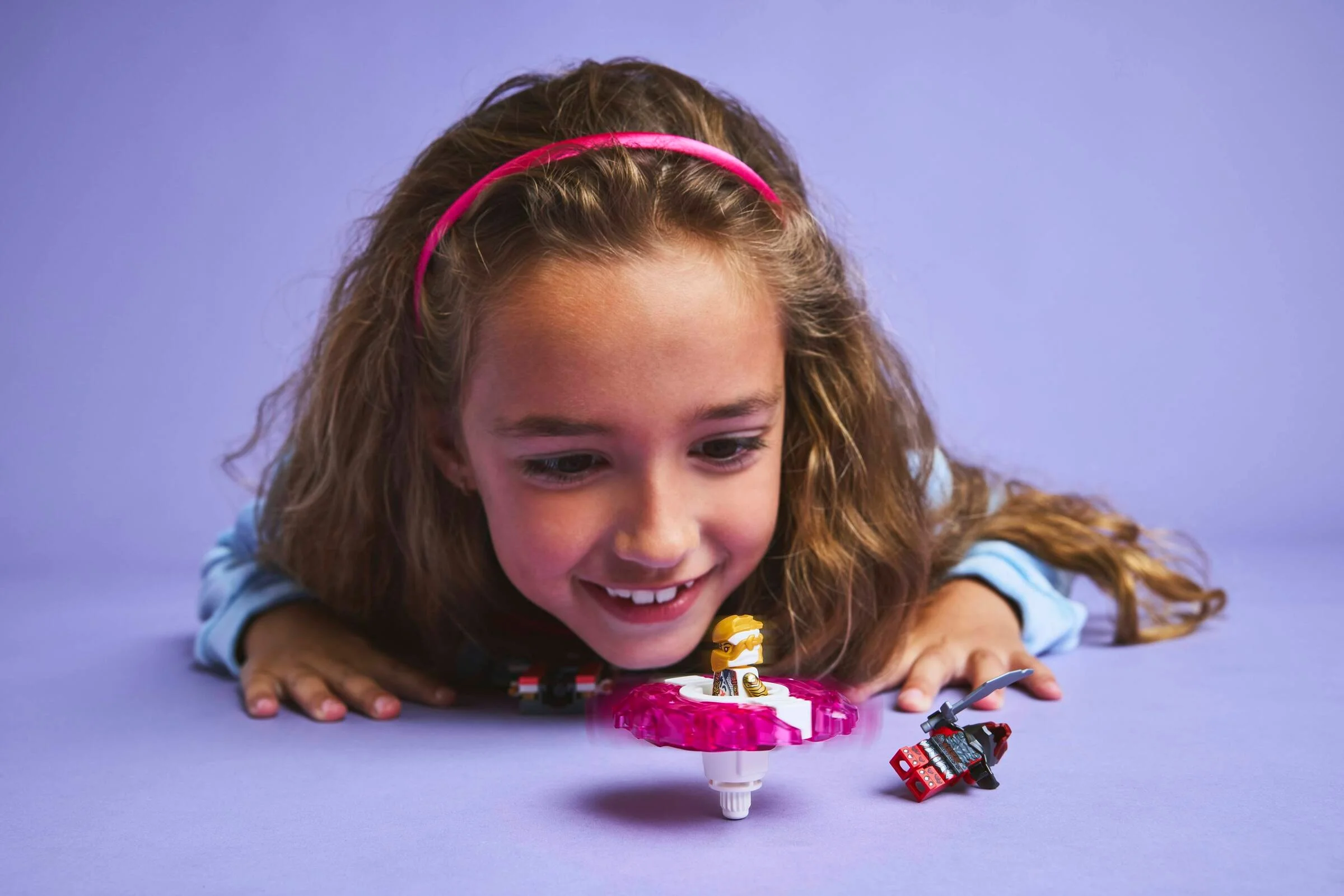 Fată zâmbind, jucându-se cu spinner-ul Spinjitzu Sora LEGO Ninjago.