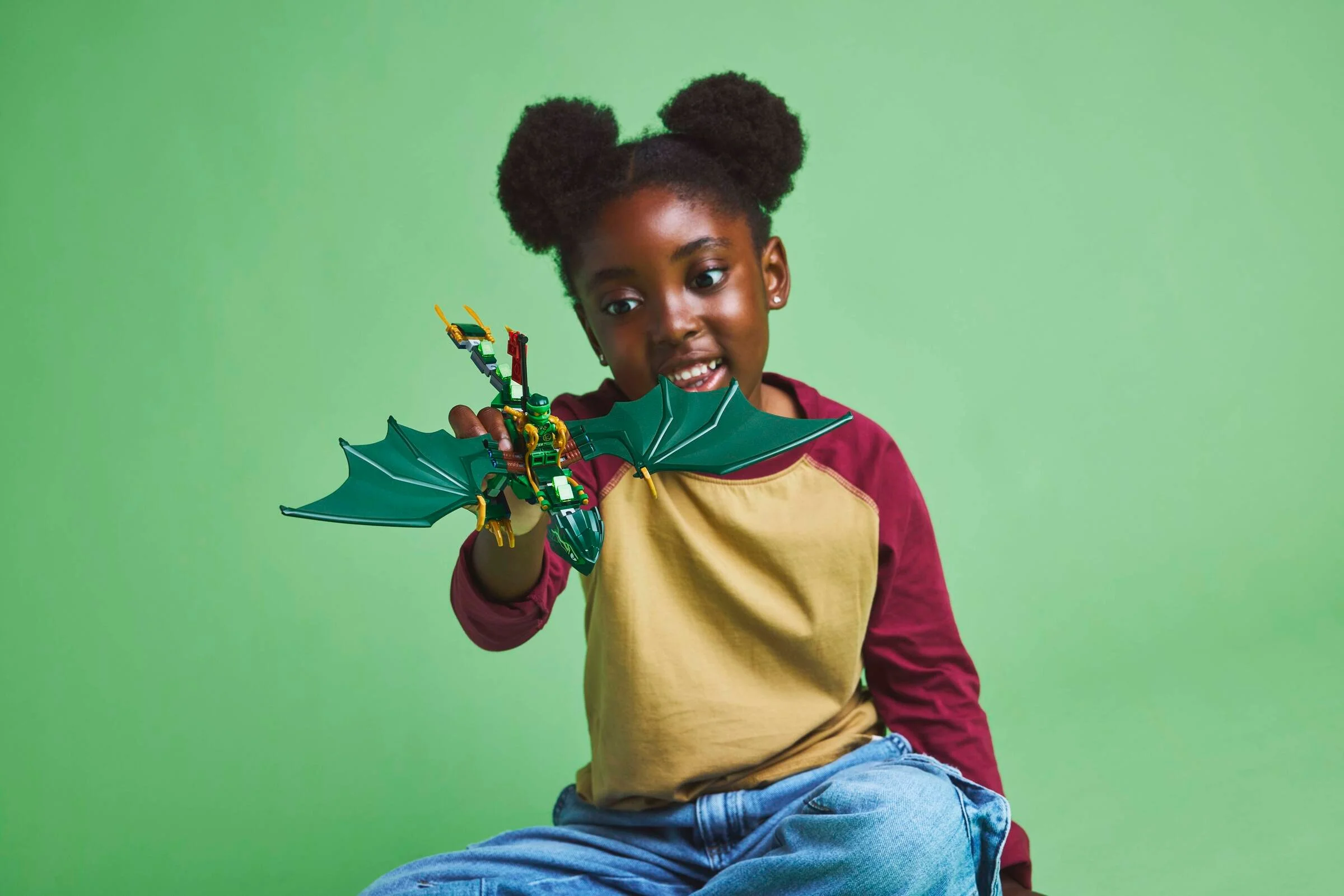 Fetiță jucându-se cu dragonul verde LEGO Ninjago. Zâmbet și entuziasm.