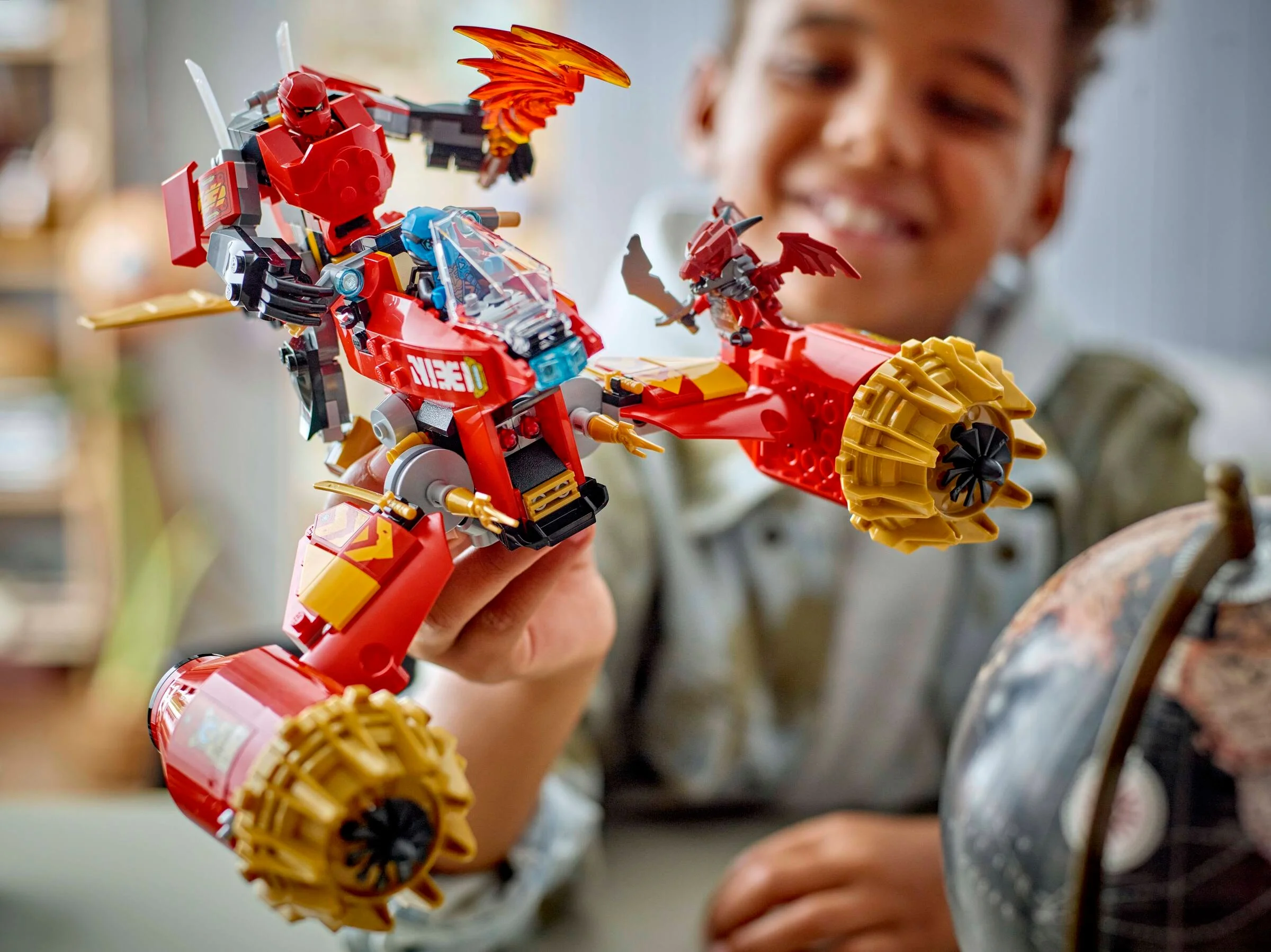 Kai's Mech Storm Rider în acțiune, un băiat zâmbind în fundal. Aventură și entuziasm!