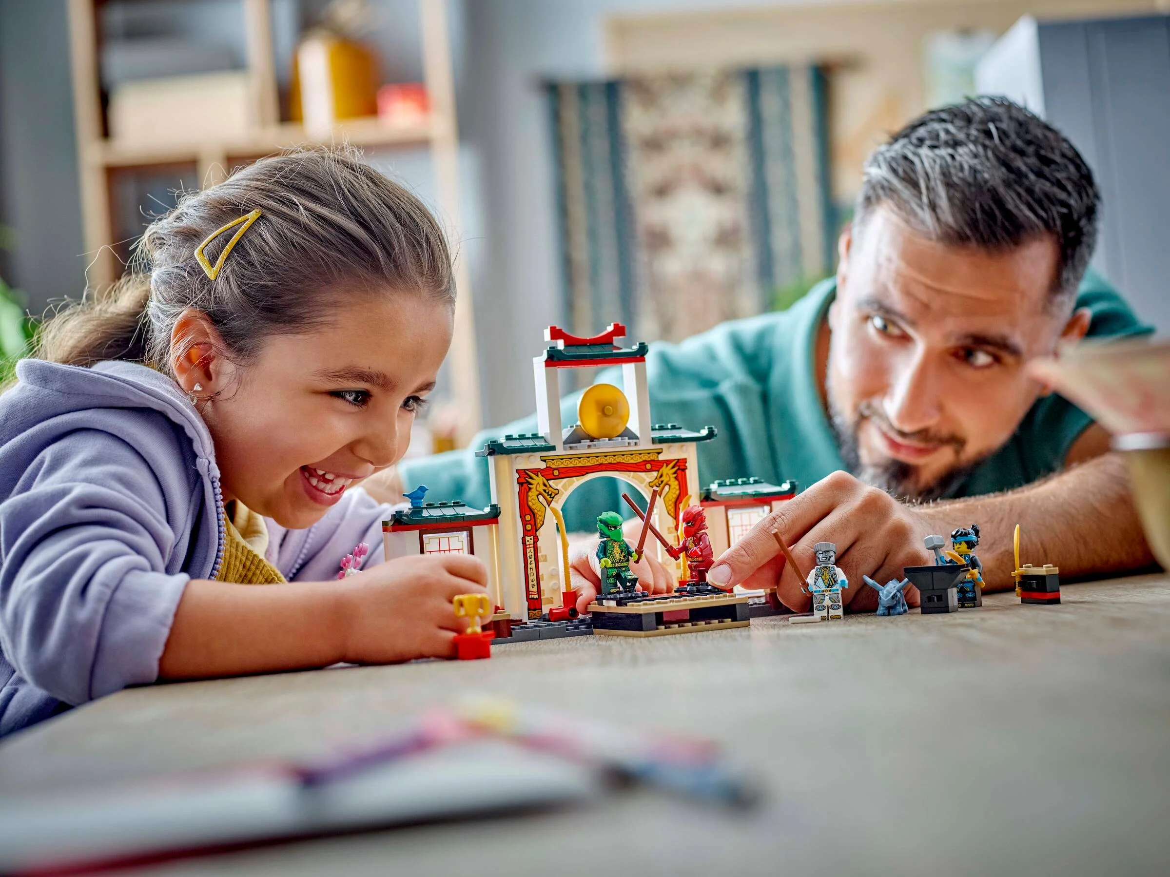 Copil și adult se joacă împreună cu templul LEGO Ninjago, zâmbete și bucurie.