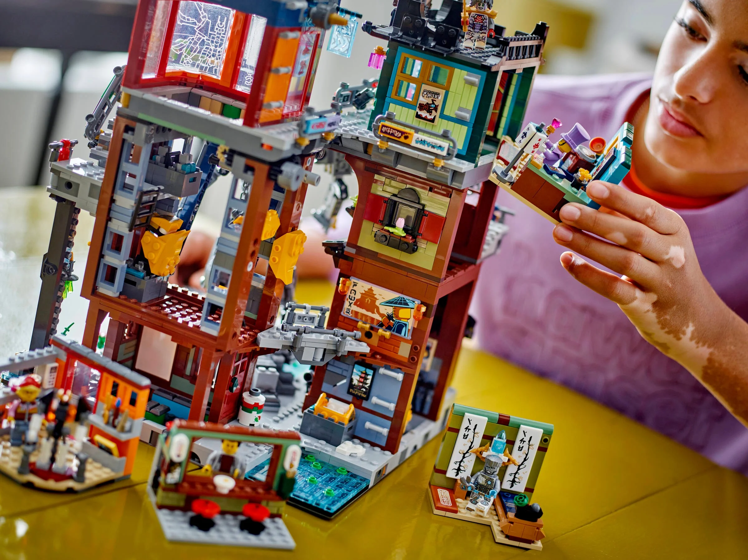 O fată admiră un modul LEGO din setul NINJAGO City Workshops. Detaliile clădirii sunt vizibile.