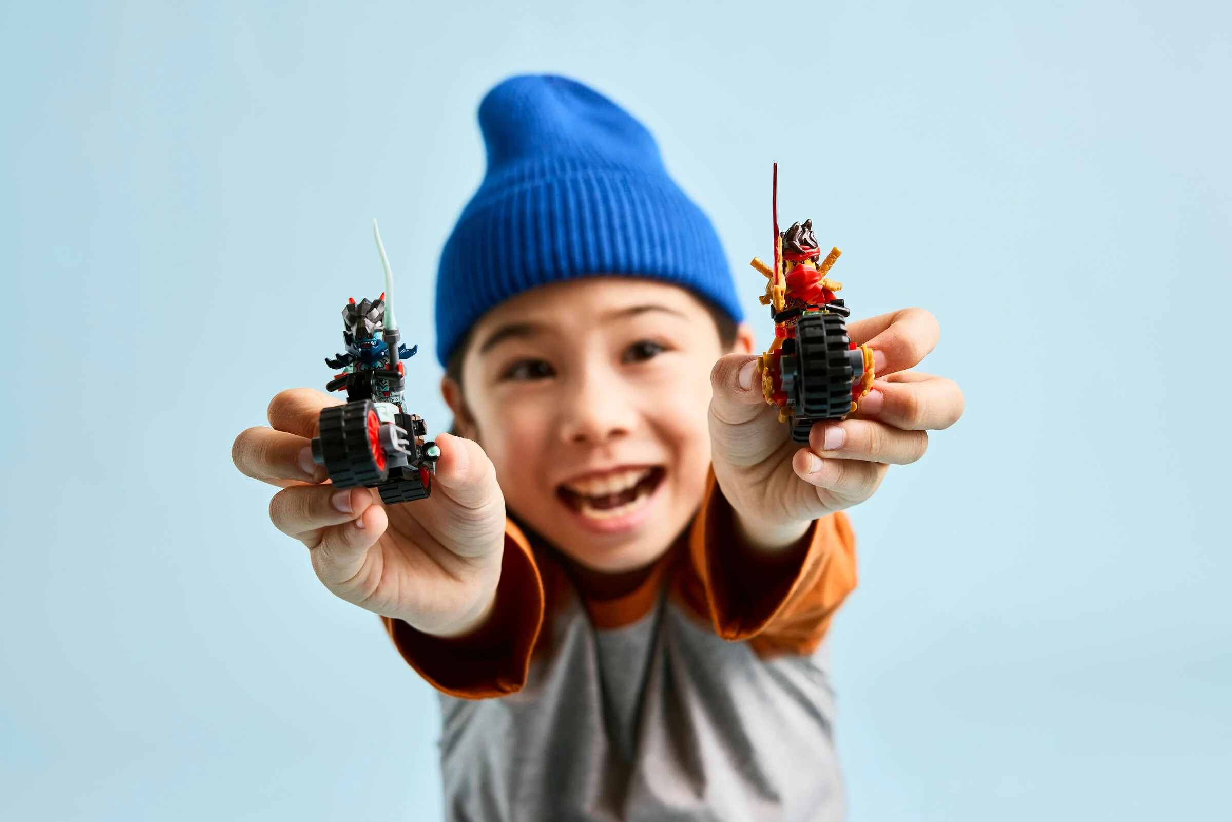 Copil zâmbitor prezintă motocicletele LEGO Ninjago într-o imagine plină de bucurie.