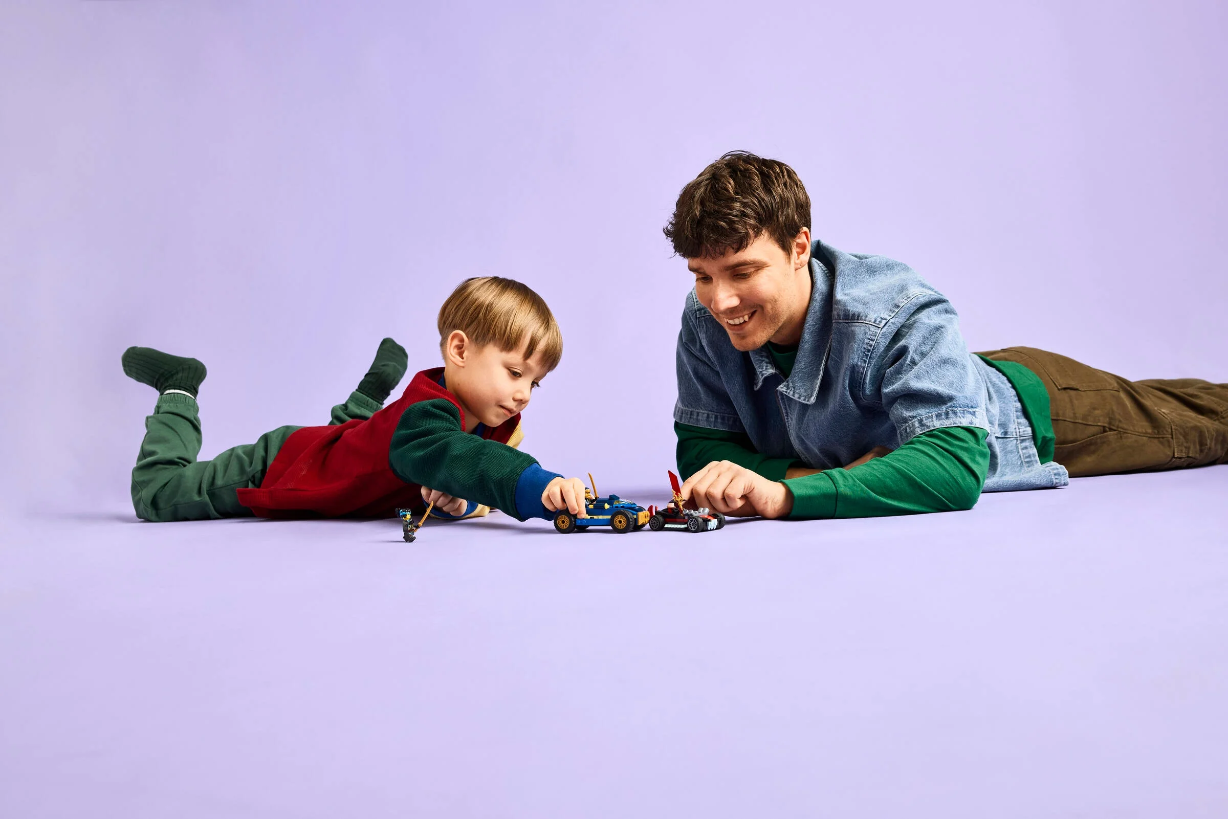Un tată și fiu se joacă cu mașinile LEGO Ninjago, zâmbitori și relaxați.