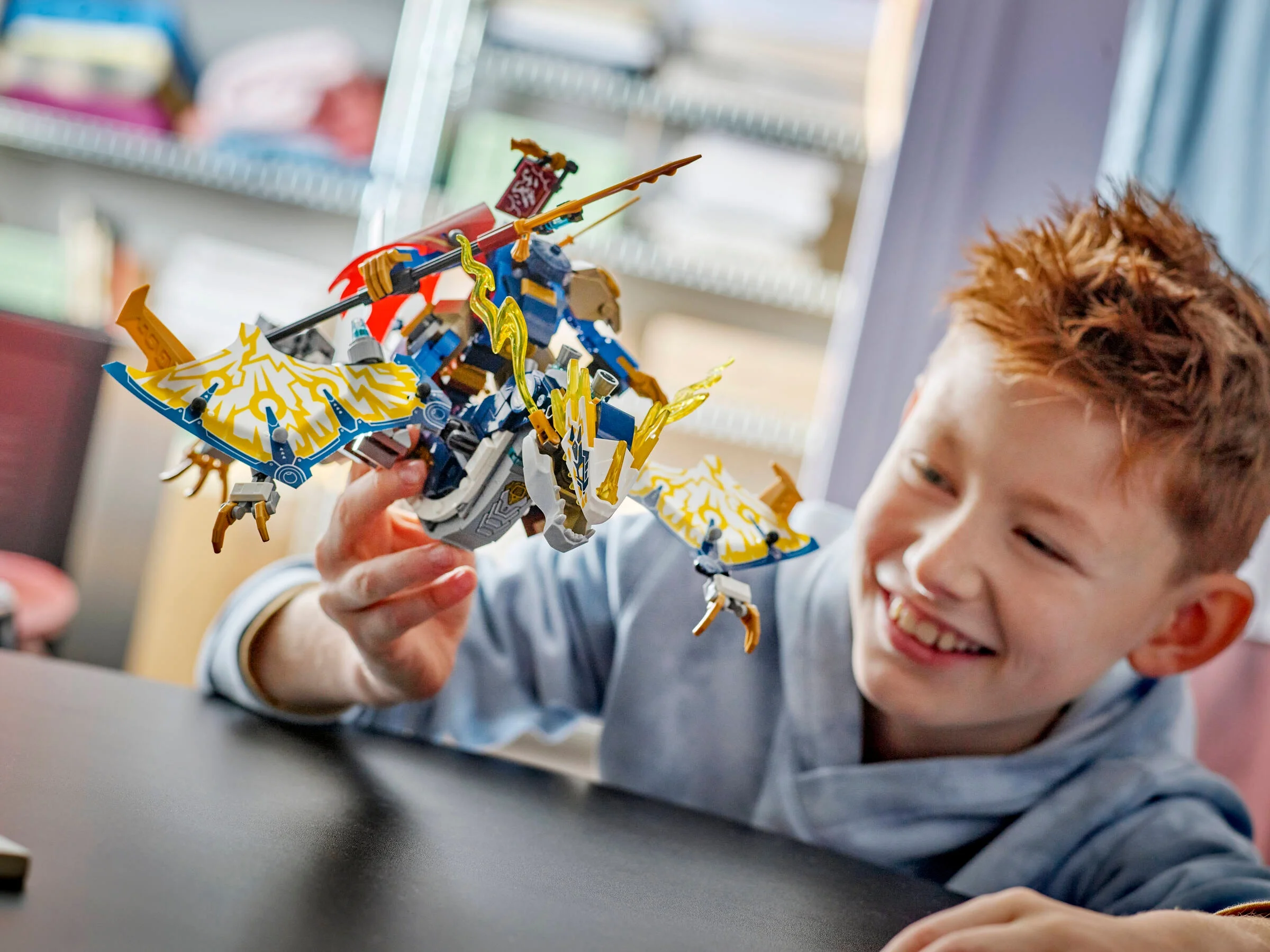 Băiat zâmbitor ținând în mână dragonul-robot NINJAGO 71843. E bucuros și pare că se joacă.