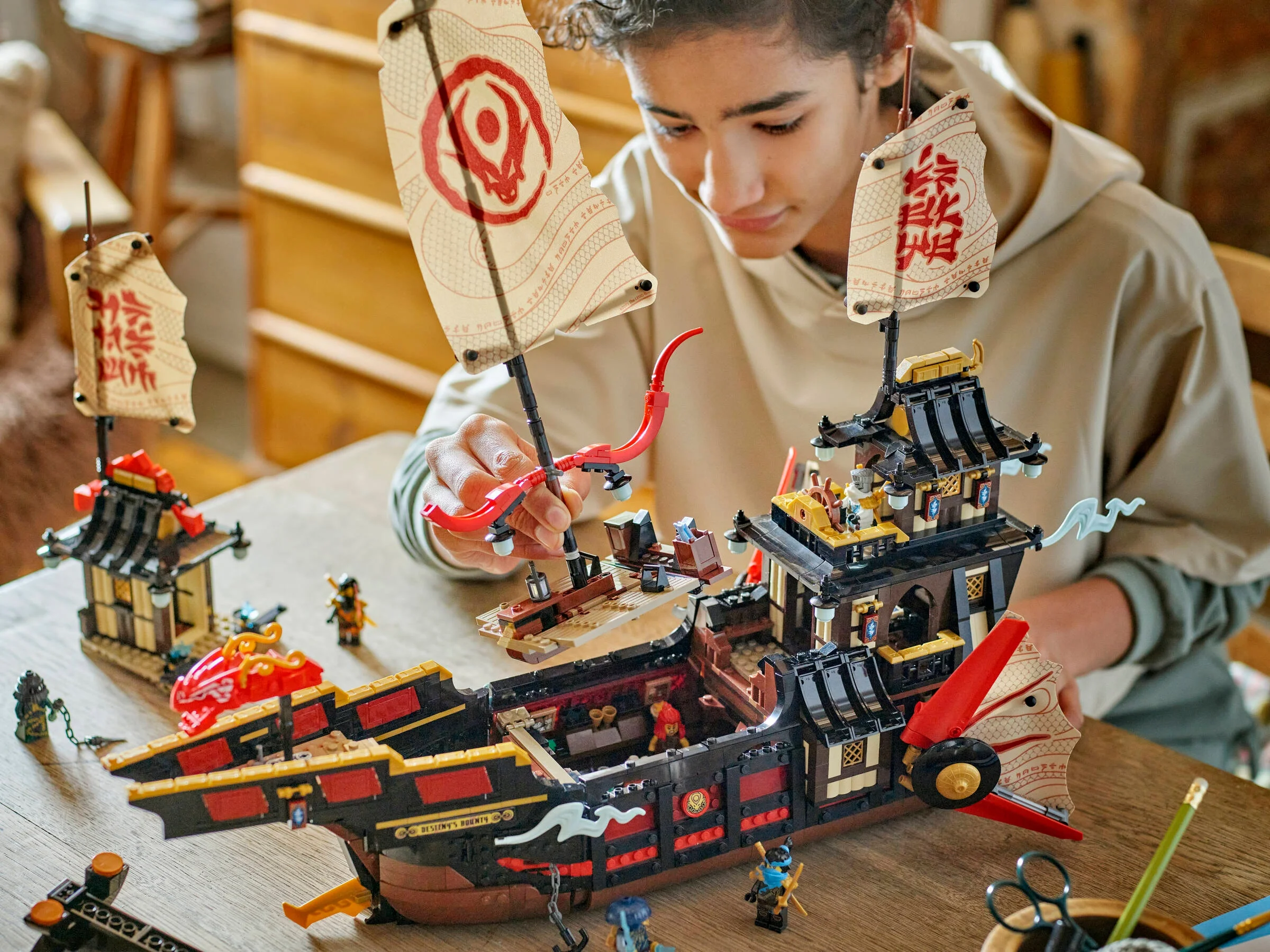Băiat asamblând setul LEGO Ninjago 71848, Templul Bounty, la o masă.