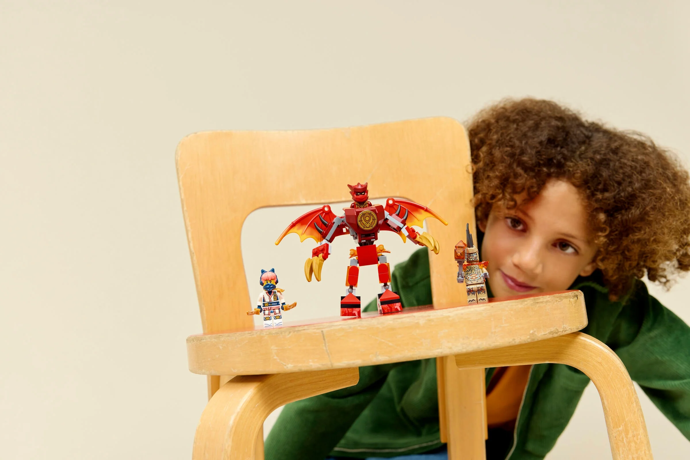 Copil se joacă cu setul LEGO Ninjago 71851, Kai's Dragon Mech Battle Pack. Mech-ul și minifigurinele sunt pe un scaun.