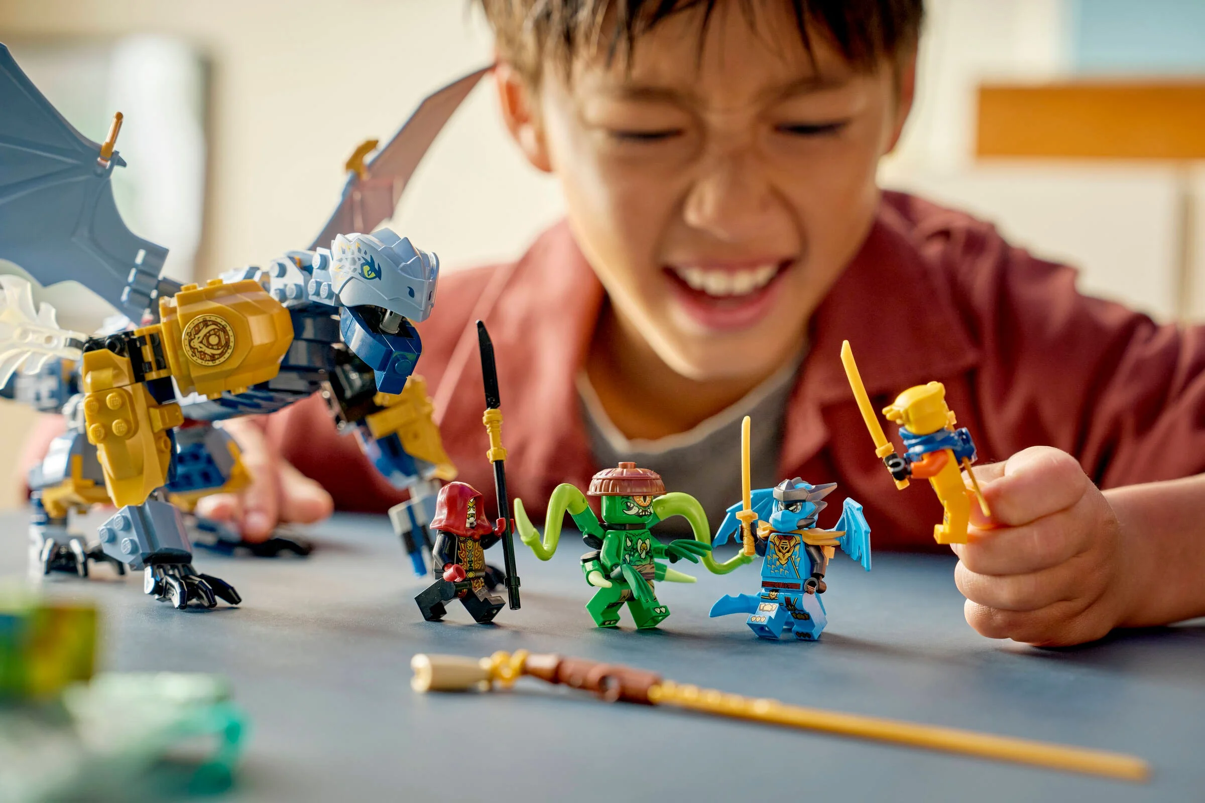 Copil zâmbind, se joacă cu dragonul Riyu și minifigurinele Ninjago.