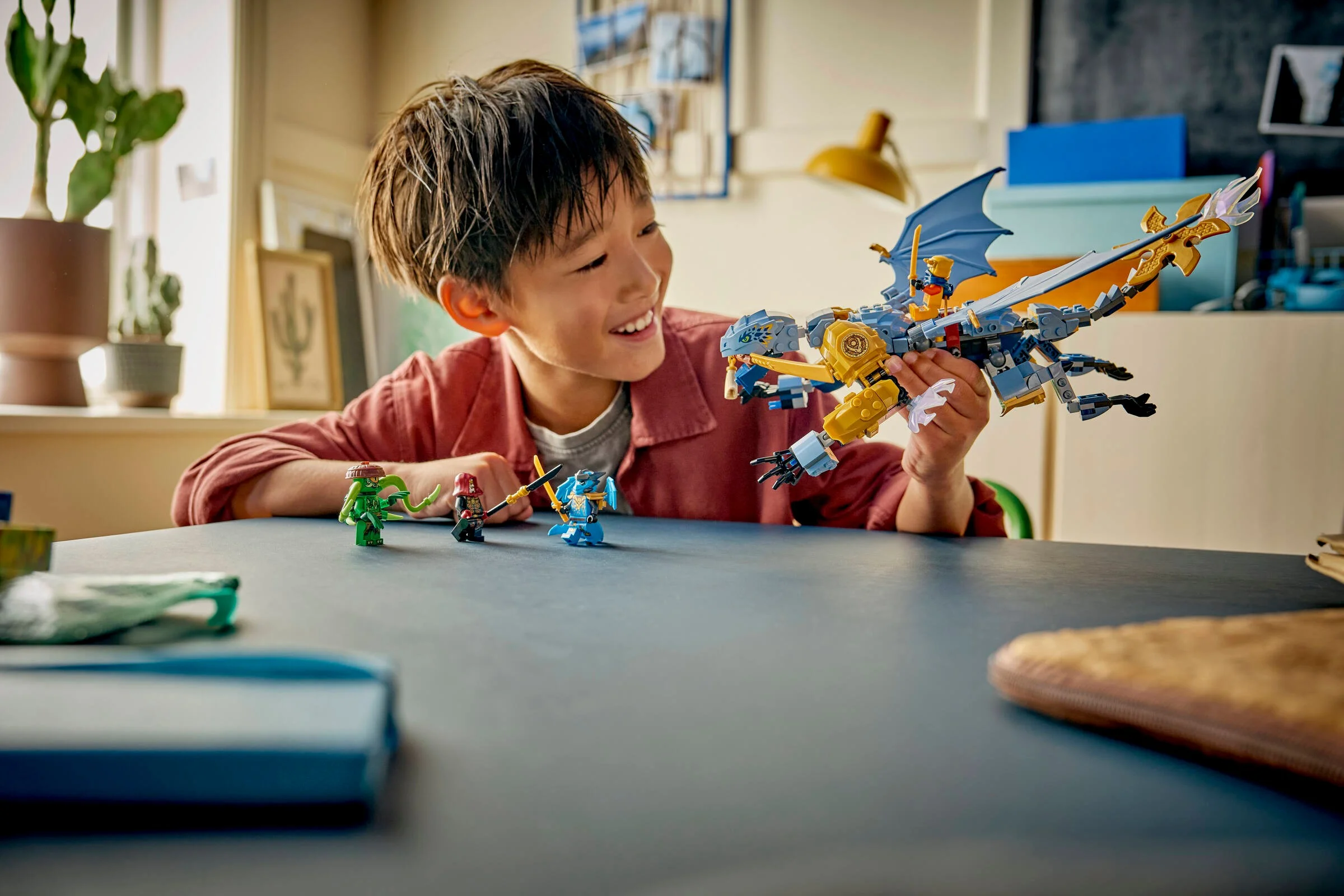 Copil zâmbind în timp ce se joacă cu dragonul Riyu și minifigurinele Ninjago.