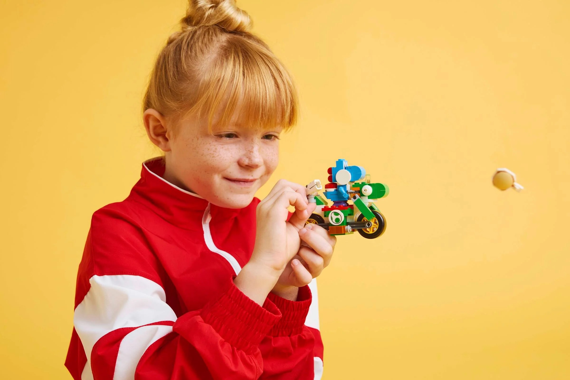 Fetiță cu un LEGO Yoshi Bike, pe fundal galben. Model colorat și distractiv.