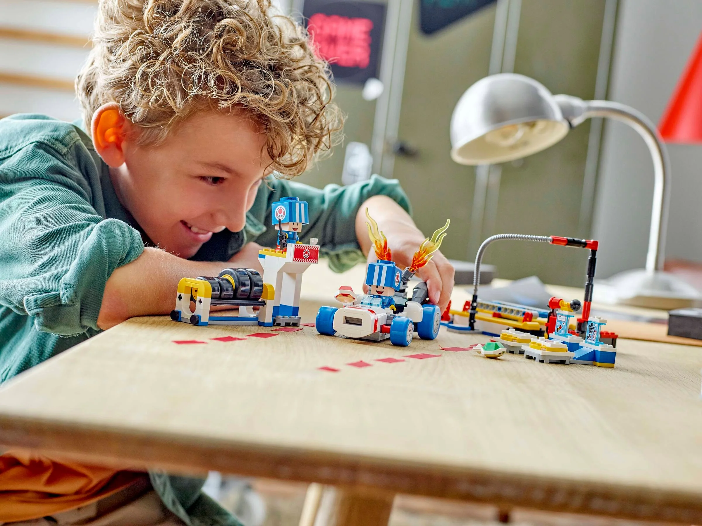 Un copil zâmbește, jucându-se cu garajul lui Toad construit din LEGO.