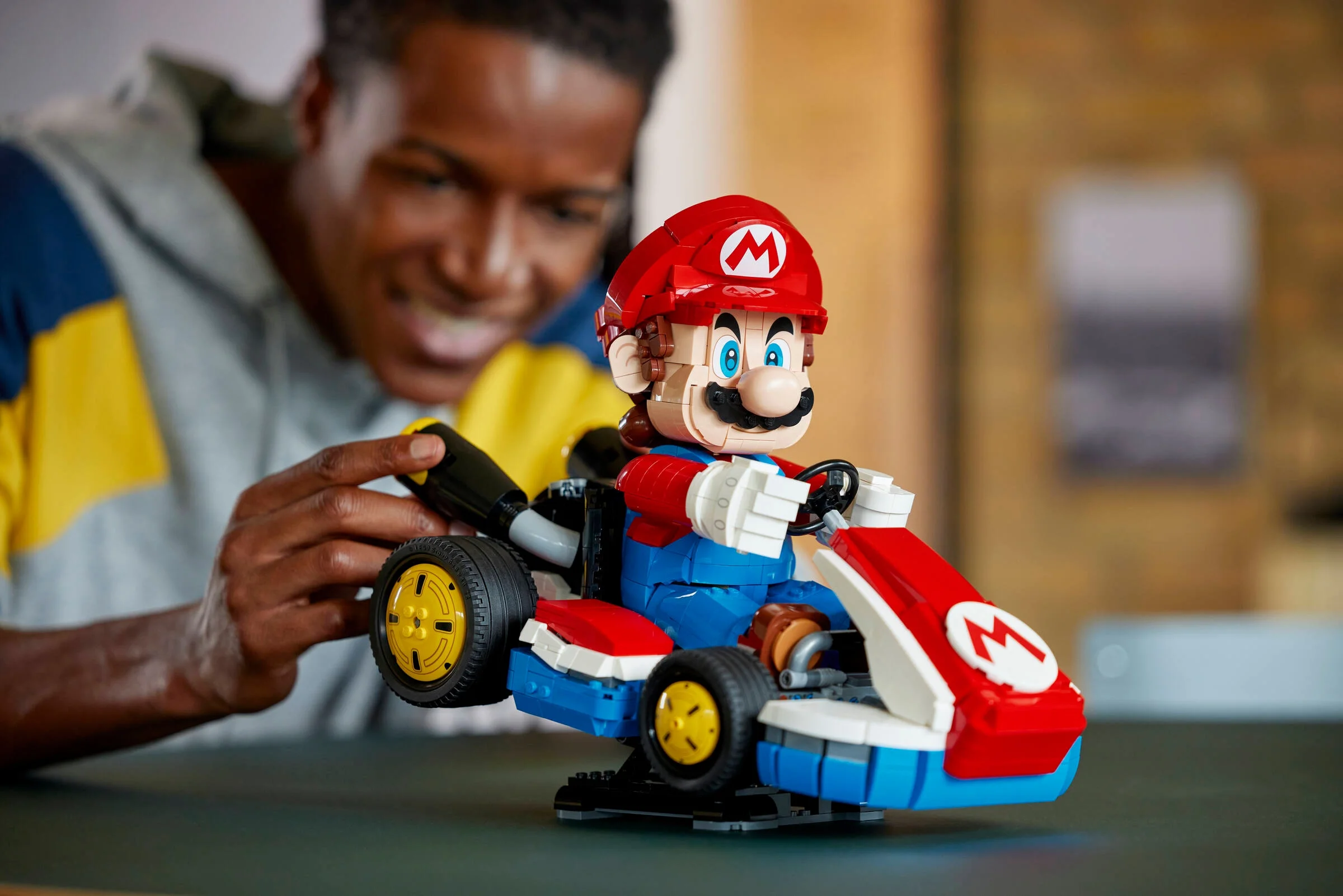 Imagine cu un bărbat zâmbind, ținând setul LEGO Mario și kartul său. Focus pe modelul construit.