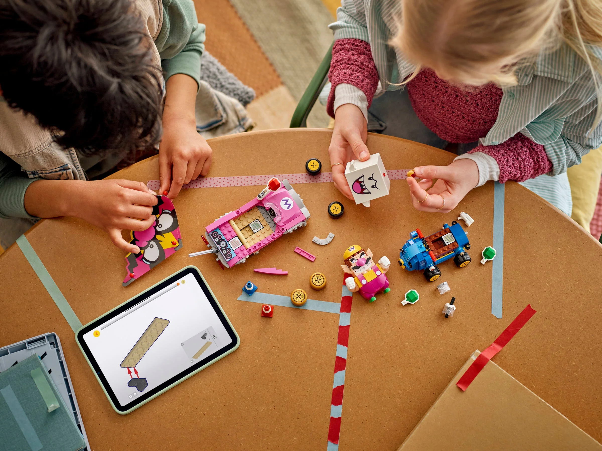 Copii construind setul LEGO 72038, Wario și King Boo, împreună, folosind o tabletă cu instrucțiuni.