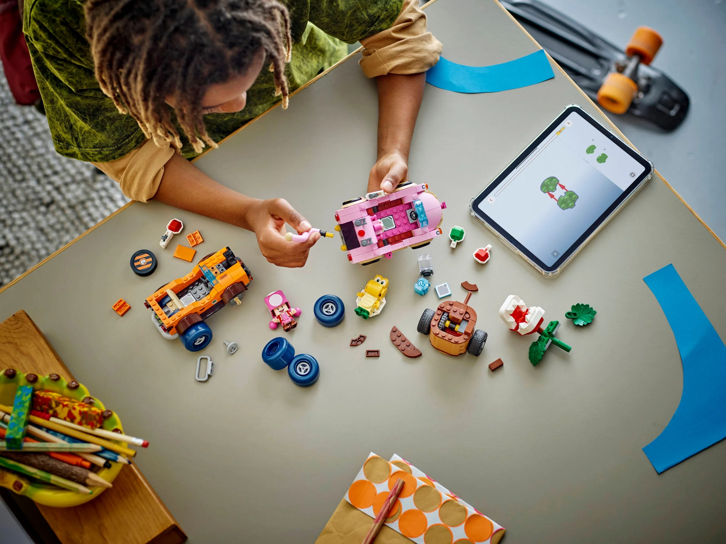 Copil construind mașinile LEGO Super Mario. Instrucțiuni pe tabletă, piesele împrăștiate pe masă.