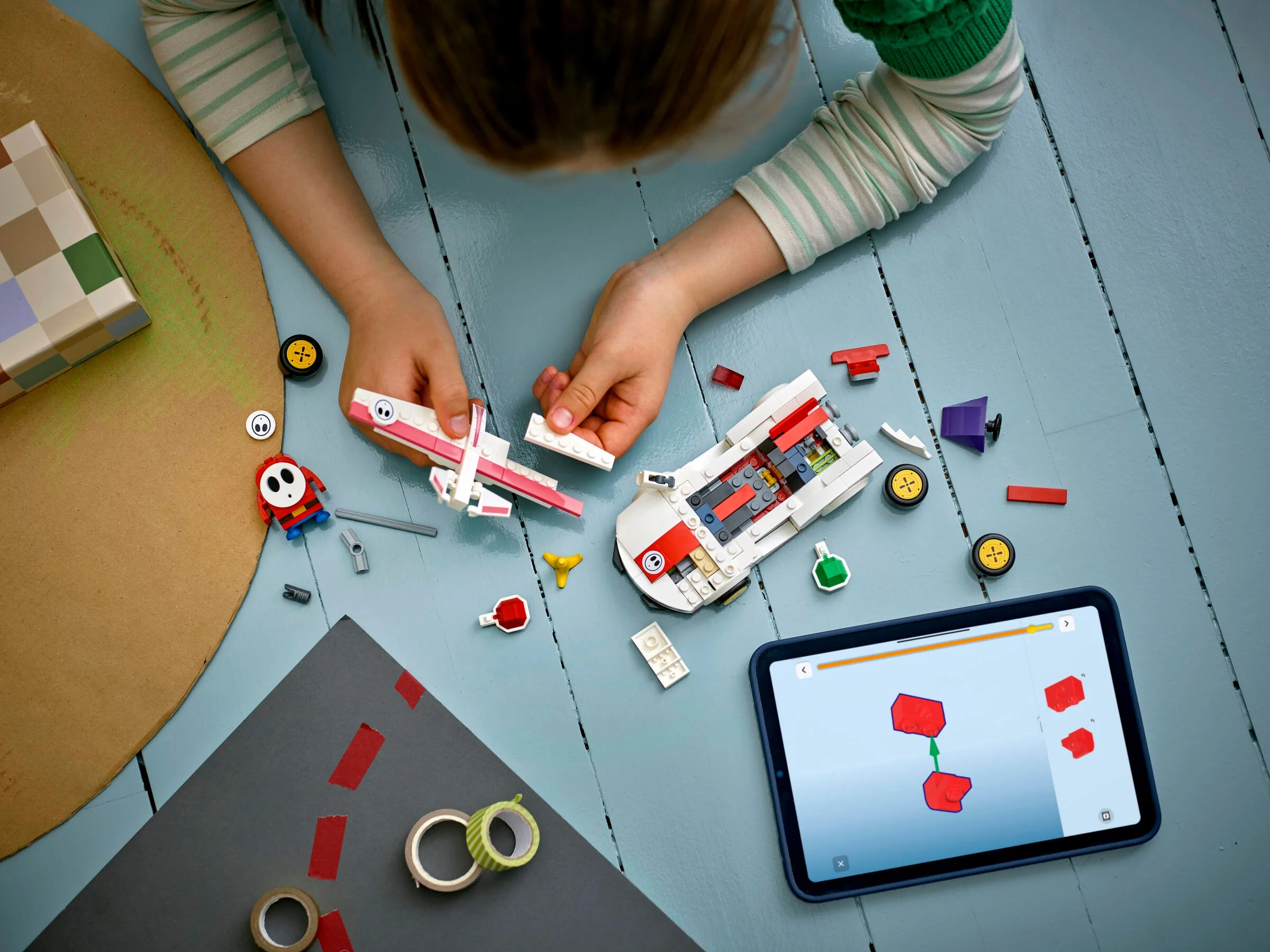 O fetiță construiește setul LEGO Super Mario Shy Guy & P-Wing folosind instrucțiuni digitale.