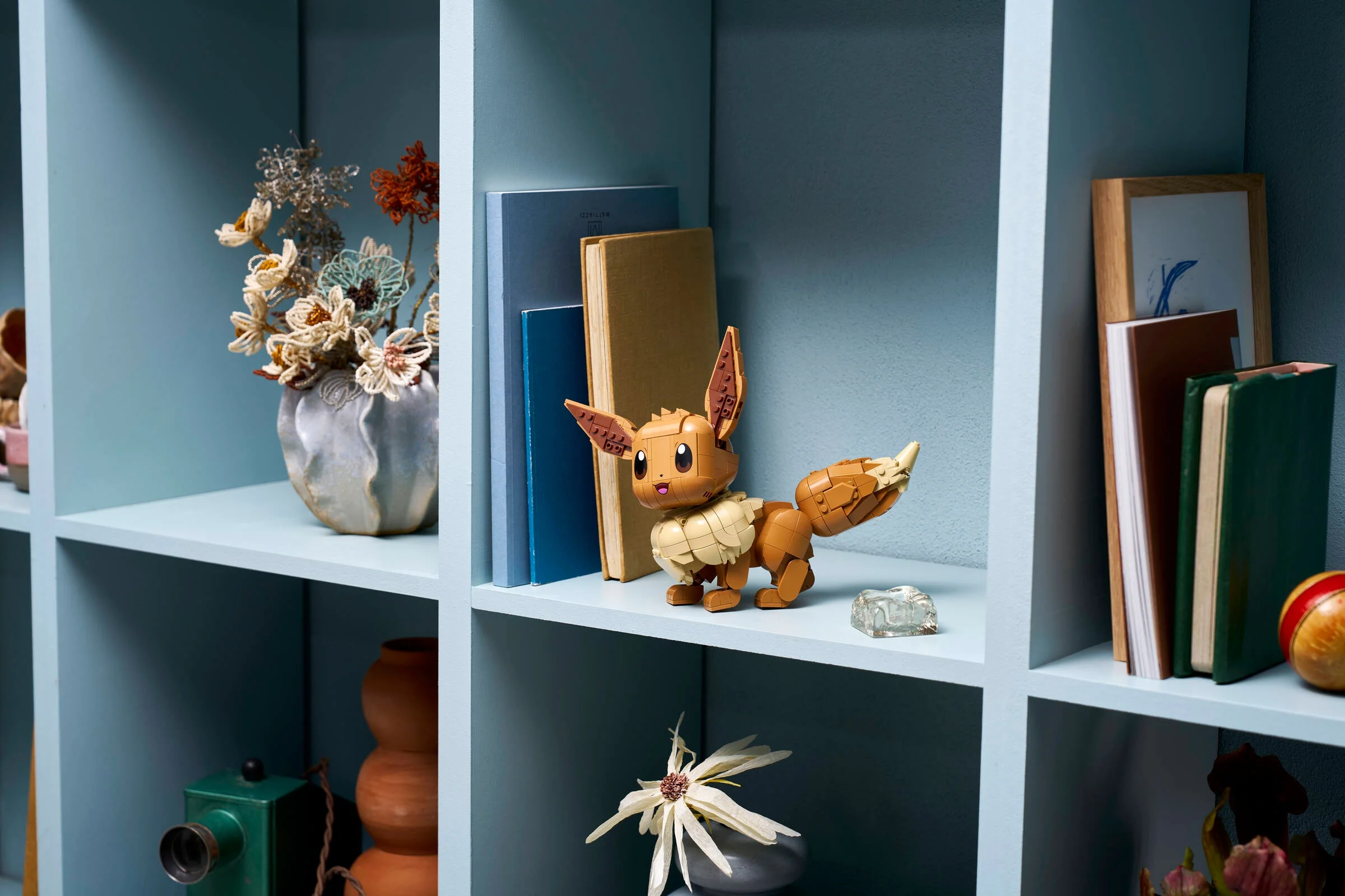 Eevee LEGO stând mândru pe o poliță, între cărți. Aspect drăguț și detaliat.