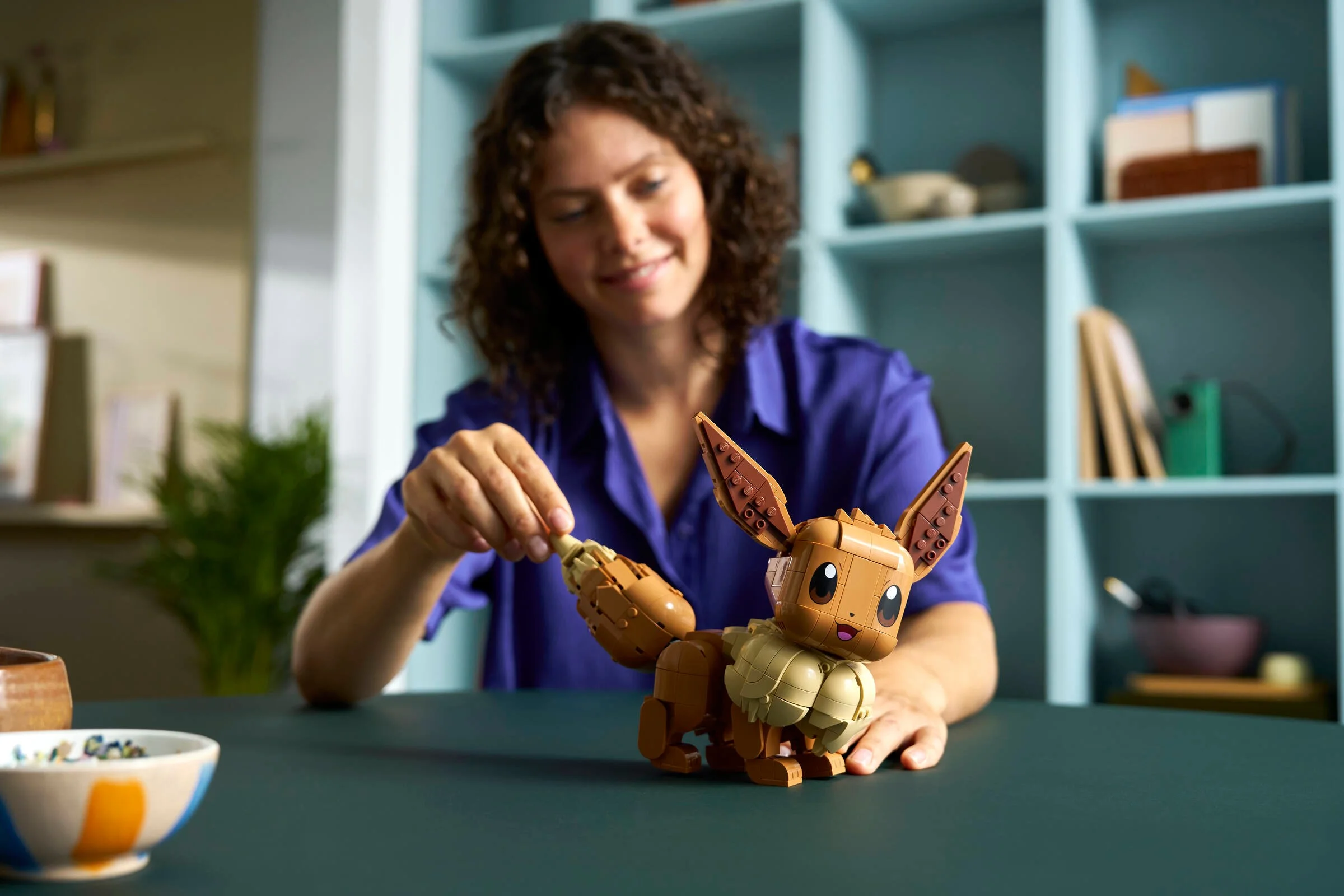 Femeie atașând coada lui Eevee LEGO. Modelul finit este vizibil, drăguț și detaliat.