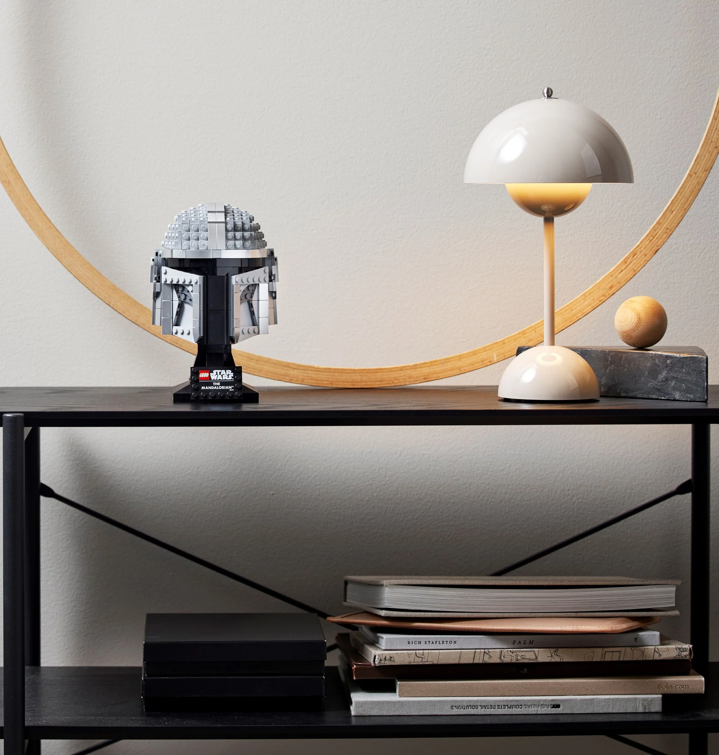 Casca Mandalorian pe un raft, decorată cu o lampă și alte obiecte decorative.