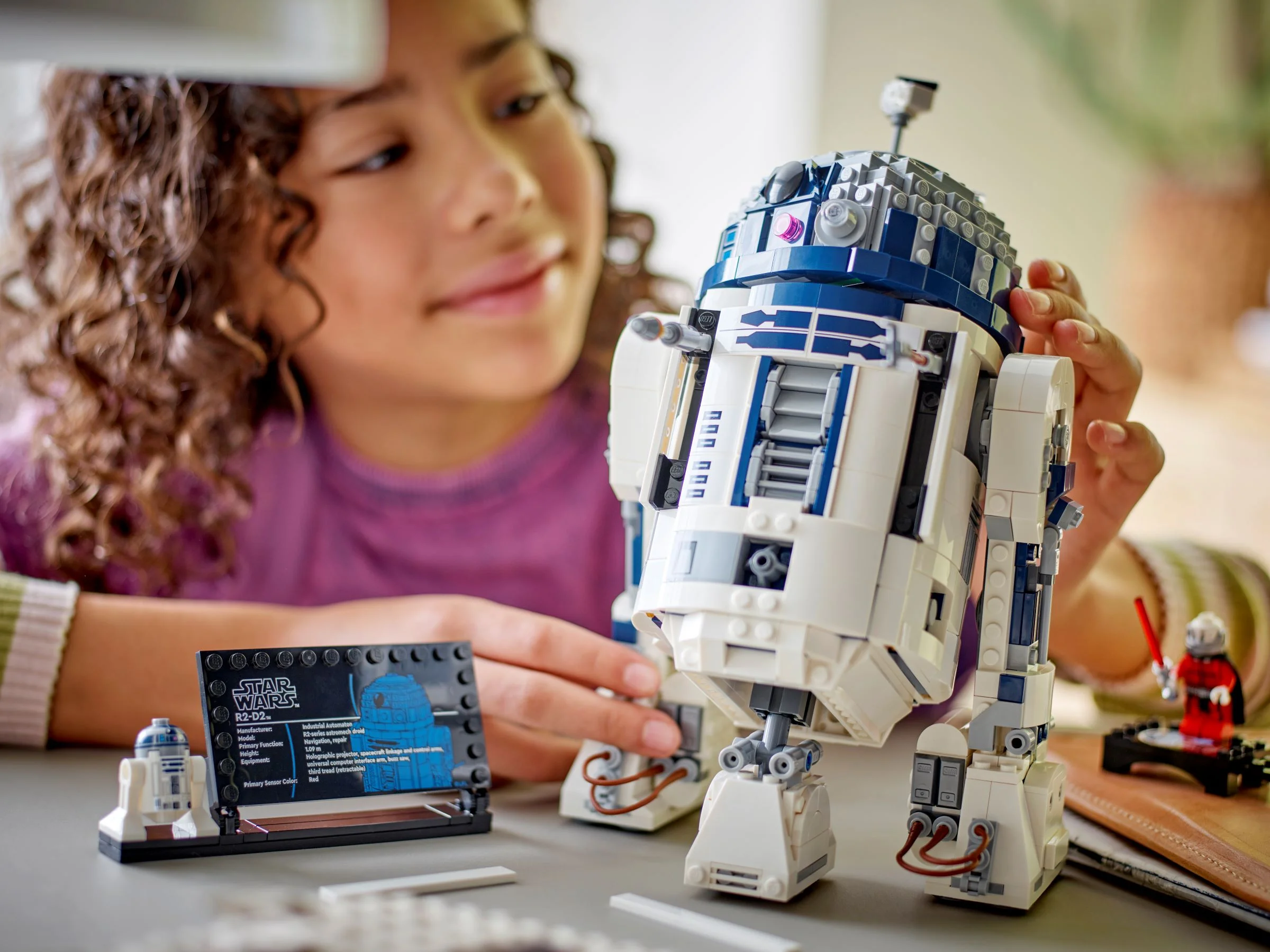 O fată interacționează cu modelul R2-D2, arătând detaliile și minifigurinele incluse.