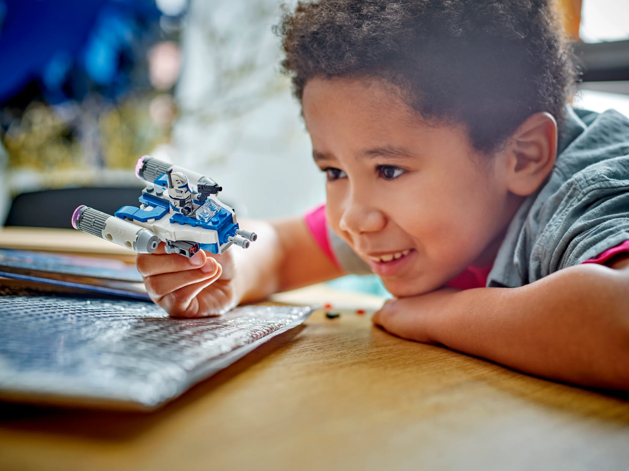 Un copil se joacă cu modelul LEGO Captain Rex Y-wing Microfighter pe o masă.