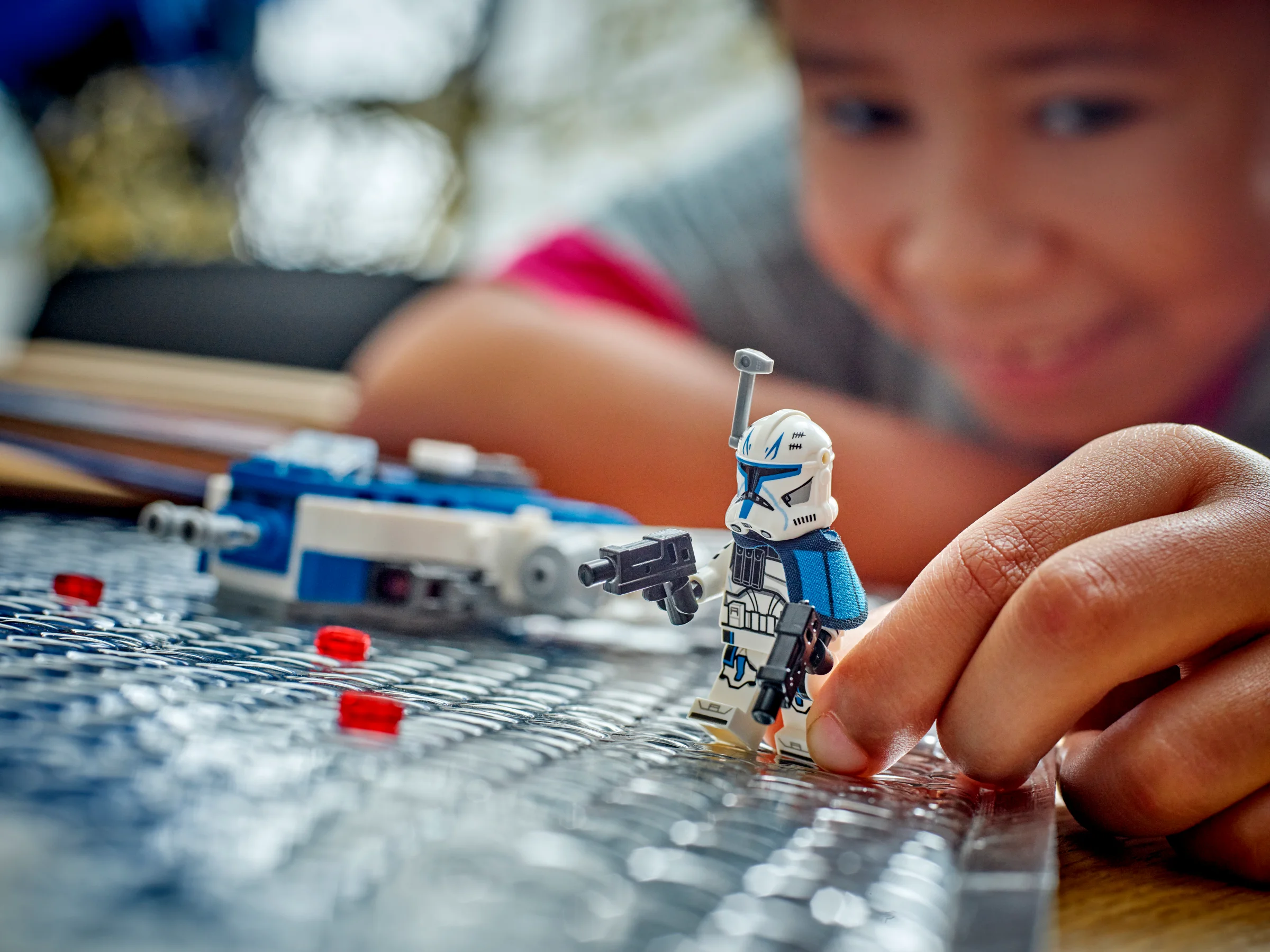 Un copil zâmbește în timp ce se joacă cu minifigurina Căpitanul Rex și Y-wing Microfighter.