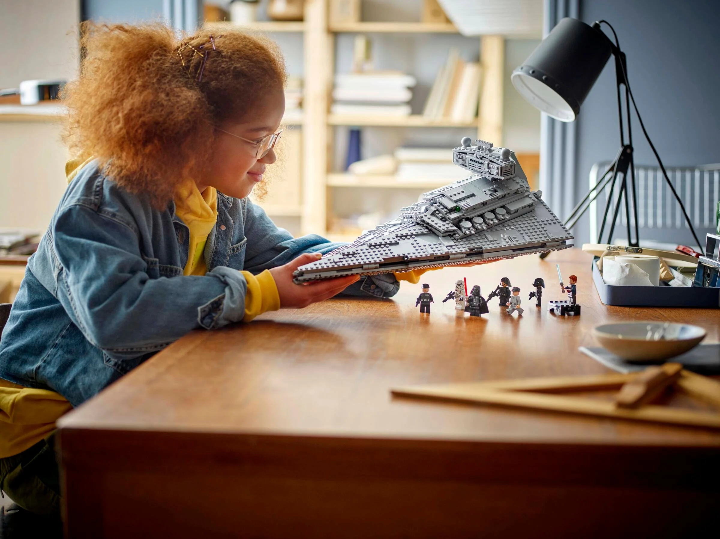 O tânără ține în mâini un Imperial Star Destroyer LEGO. Minifigurine pe masă.