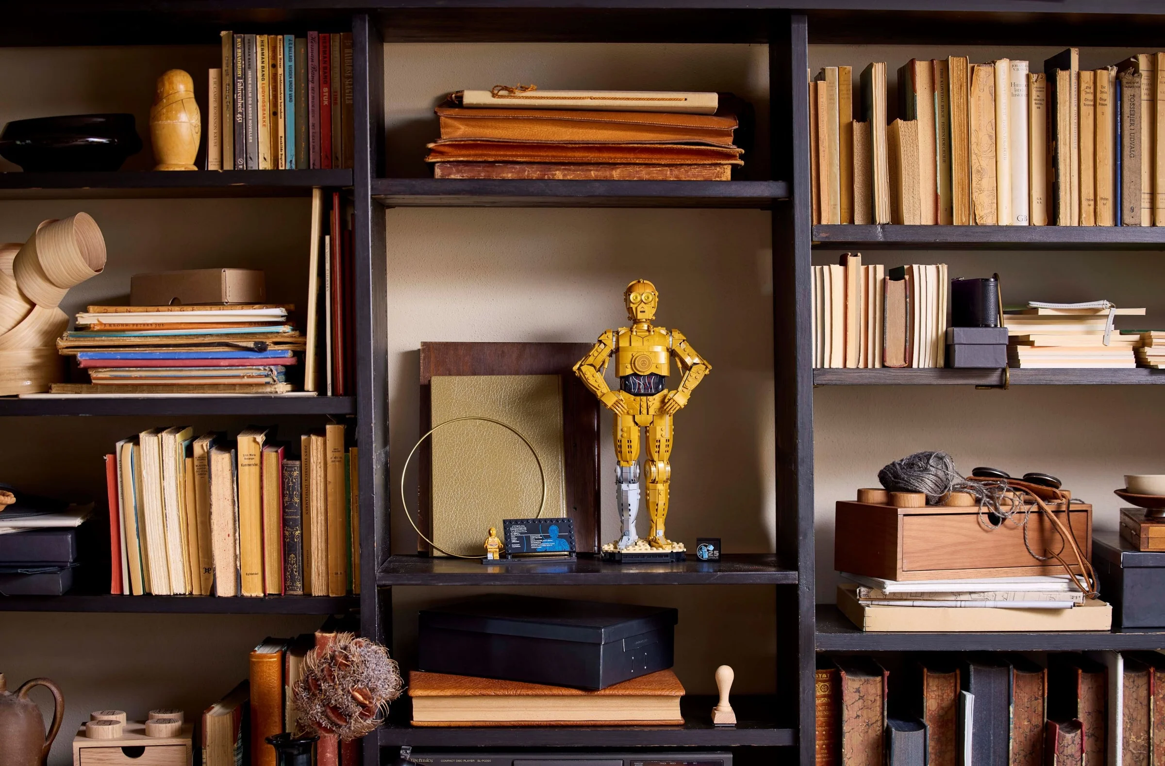 Modelul LEGO C-3PO expus pe o poliță de bibliotecă, alături de alte obiecte decorative.